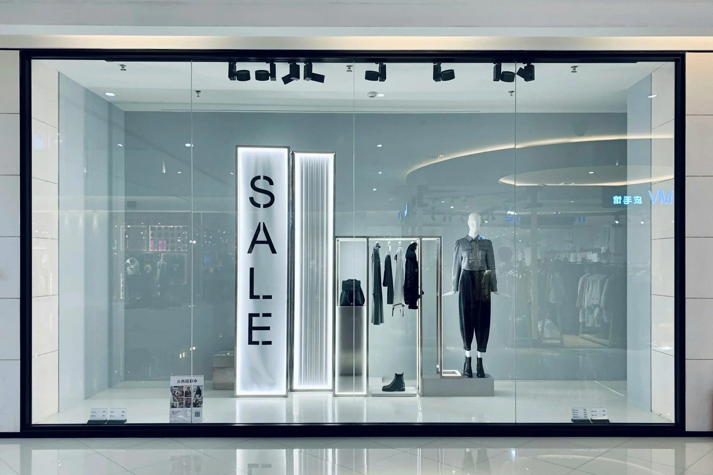 Formation Vitrine attractive. Vitrine d'un magasin de vêtements avec un panneau lumineux indiquant 'SALE', des vêtements et une mannequin habillé de noir et gris.