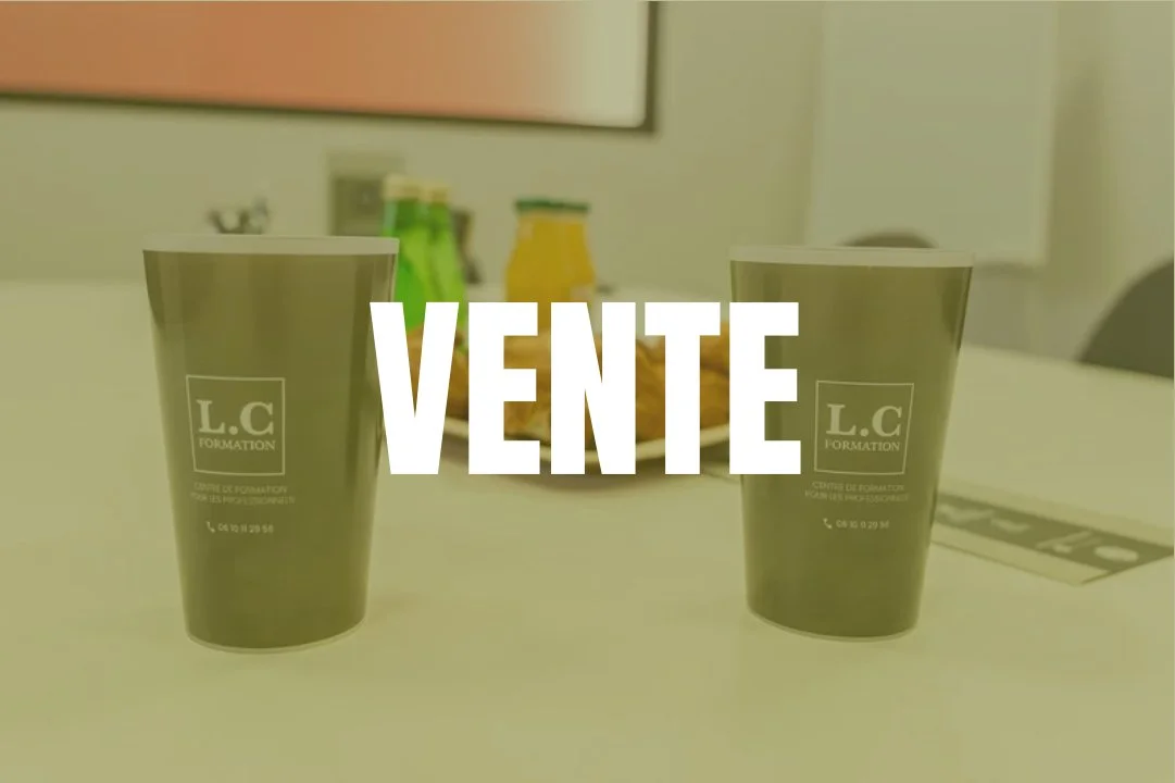 Deux gobelets en plastique gris sur une table avec le mot "VENTE" écrit en blanc au centre, en arrière-plan un plateau avec des bouteilles et un verre.