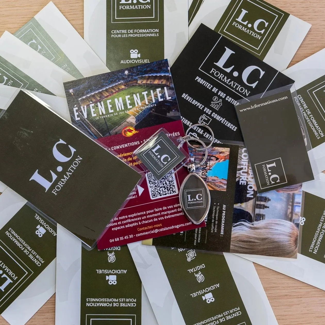 Diffuseurs de flyers, cartes de visite et objets promotionnels de 'L.C Formation', une centre de formation professionnelle. Inclut une brochure d'événements, une clé USB, et un badge.