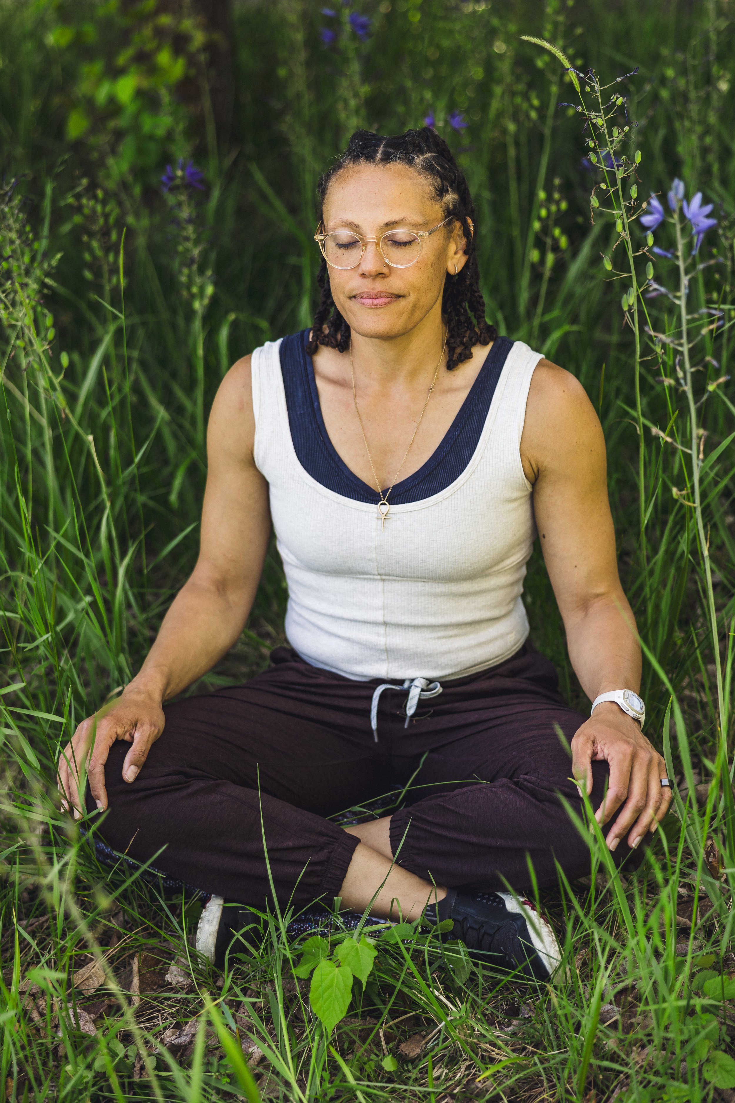 Shirley Brown practicing meditation in a lush green outdoor setting surrounded by tall grass and purple wildflowers.
