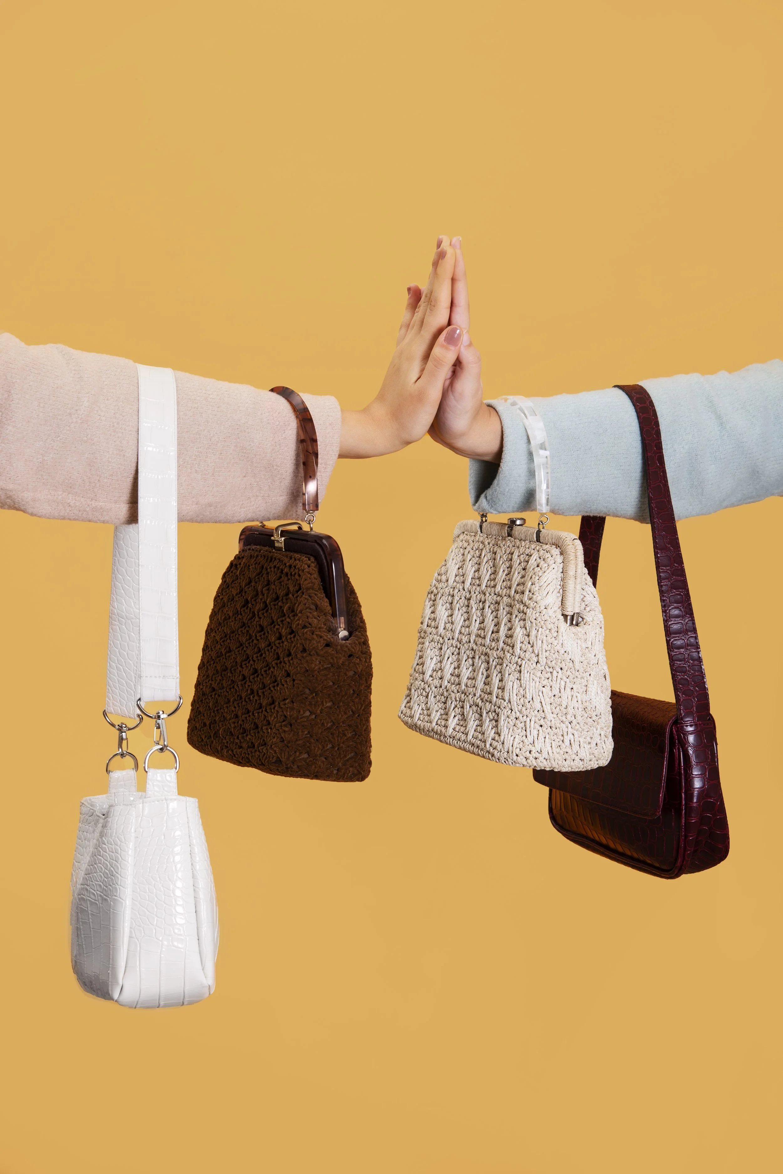 Two people giving each other a high five, each holding a variety of handbags against a yellow background.