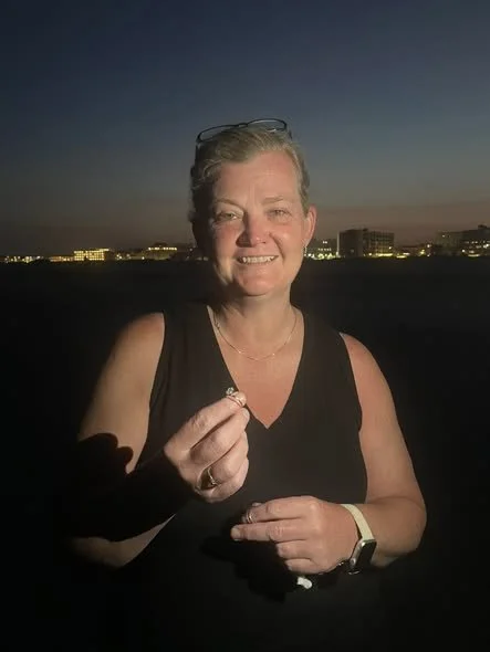 Smiling woman holding a ring outdoors at dusk with city lights in the background.