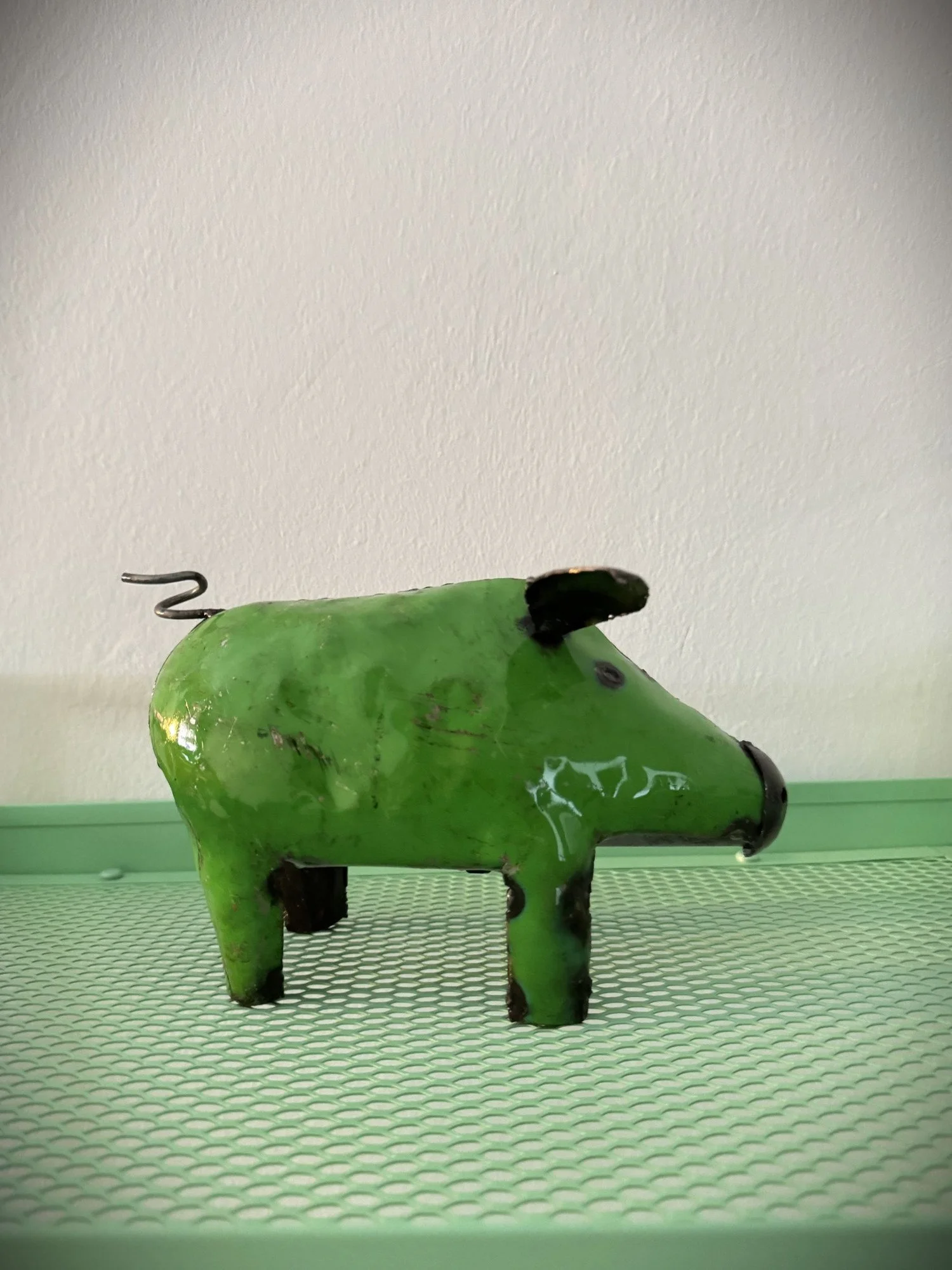 Eine skurrile Figur eines grünen Tieres mit schwarzem Kopf und Ohren, Metallhintergrund, auf grünem Gitterboden.