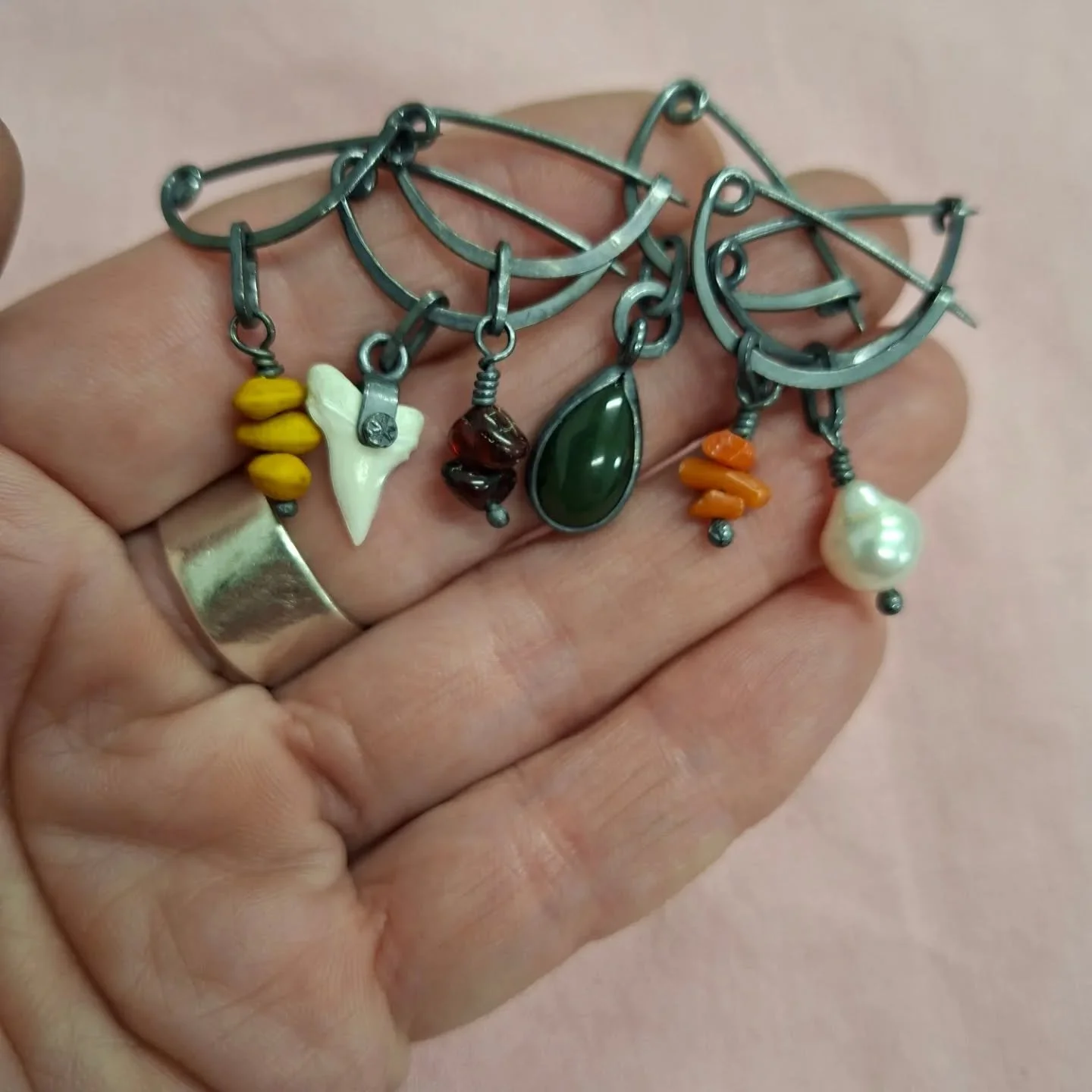 Fibulae.

Sterling silver, oxidised and shiny. Coral, amber, kōwhai seeds, shark teeth, pearl, pounamu, found safety pin.

The fibula is an early brooch or pin. 
I think mine are a bit smaller than the original ones, which were used to fasten  clothi