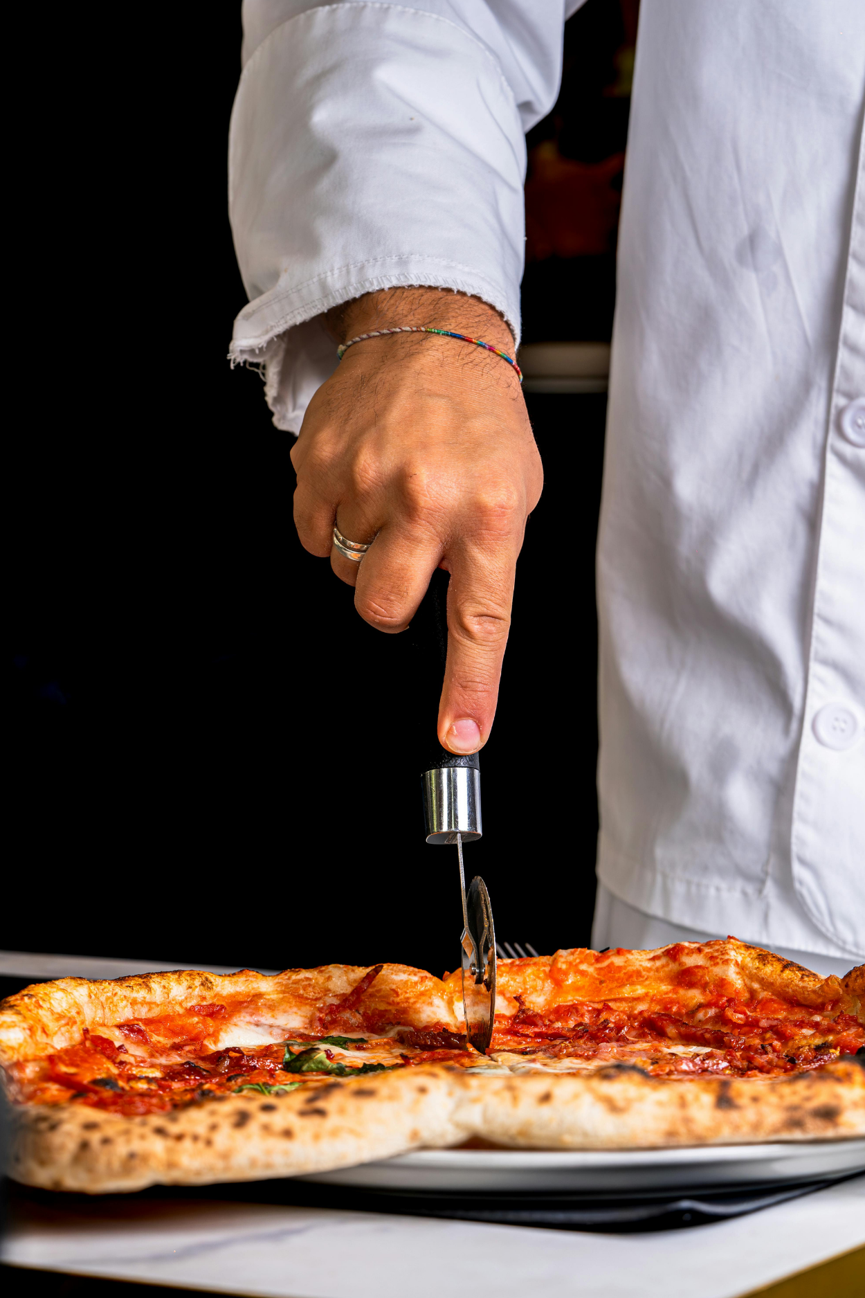 Person in a white chef's coat slicing a pizza with a pizza cutter.