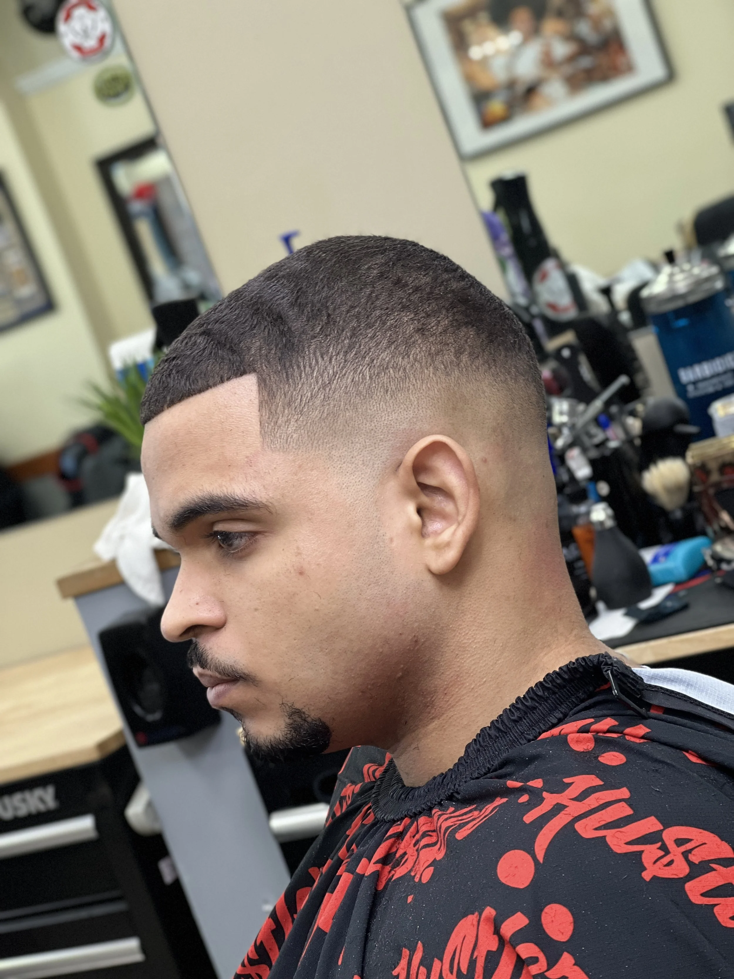 Young man with a fresh, detailed buzz cut hairstyle sitting in a barbershop.
