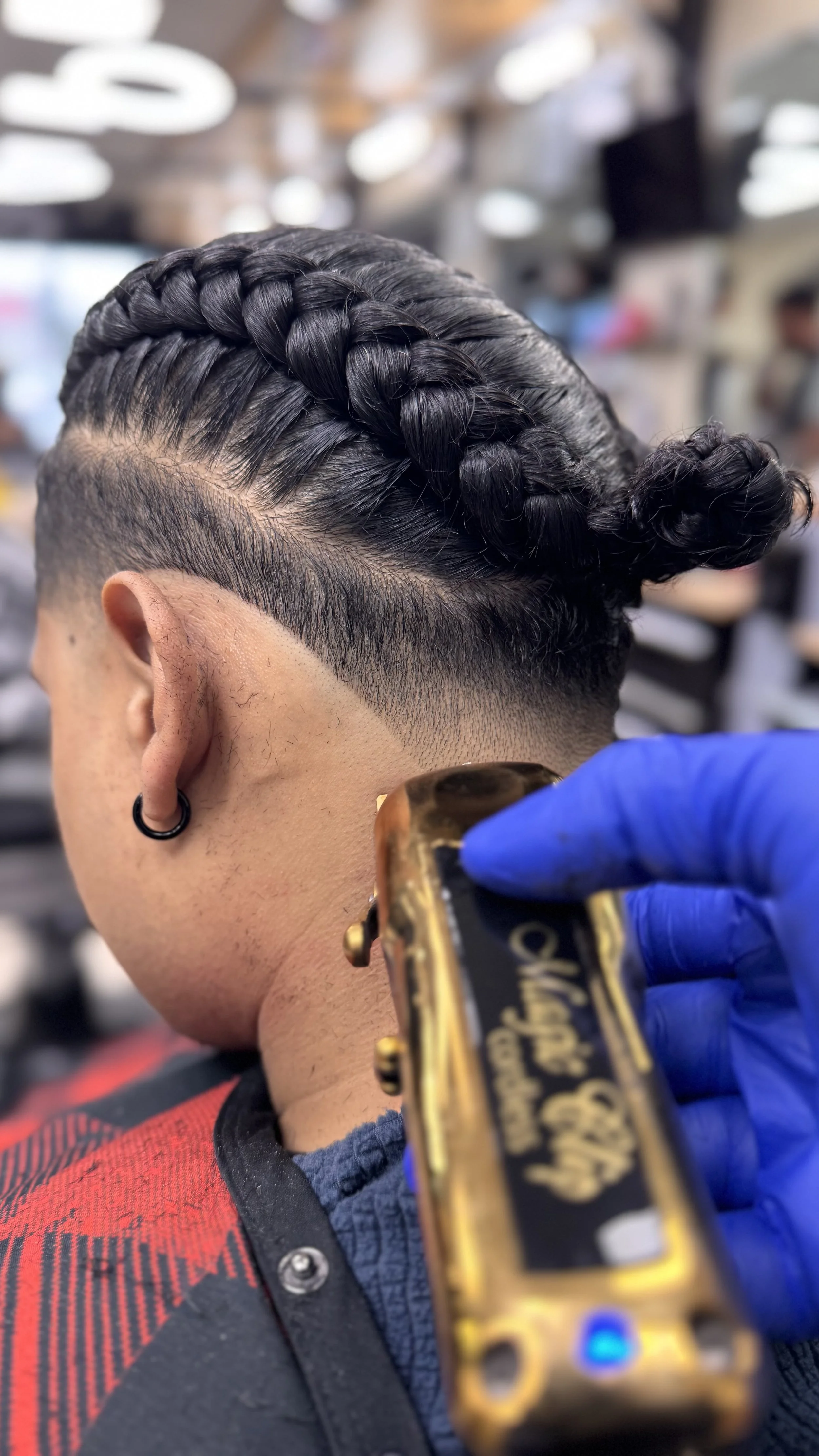 Close-up of a person getting a fade haircut with a flat top and a braided section, barber using clippers with a gold-colored handle.