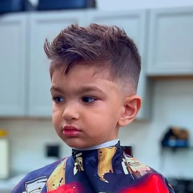 Young boy with styled hair getting a haircut at a barbershop.