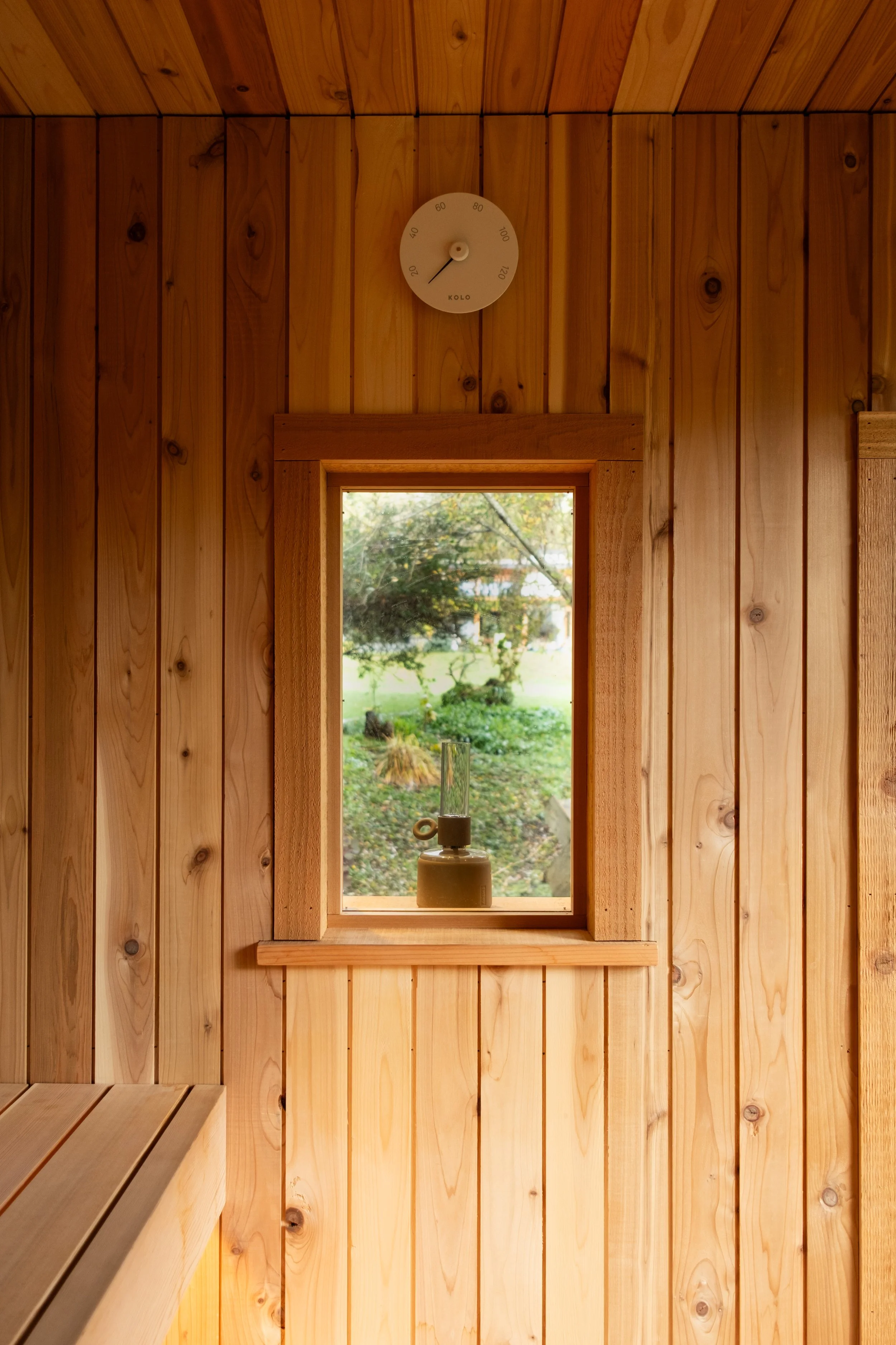 Wood-paneled interior with a small rectangular window, a stool, and a thermometer on the wall.