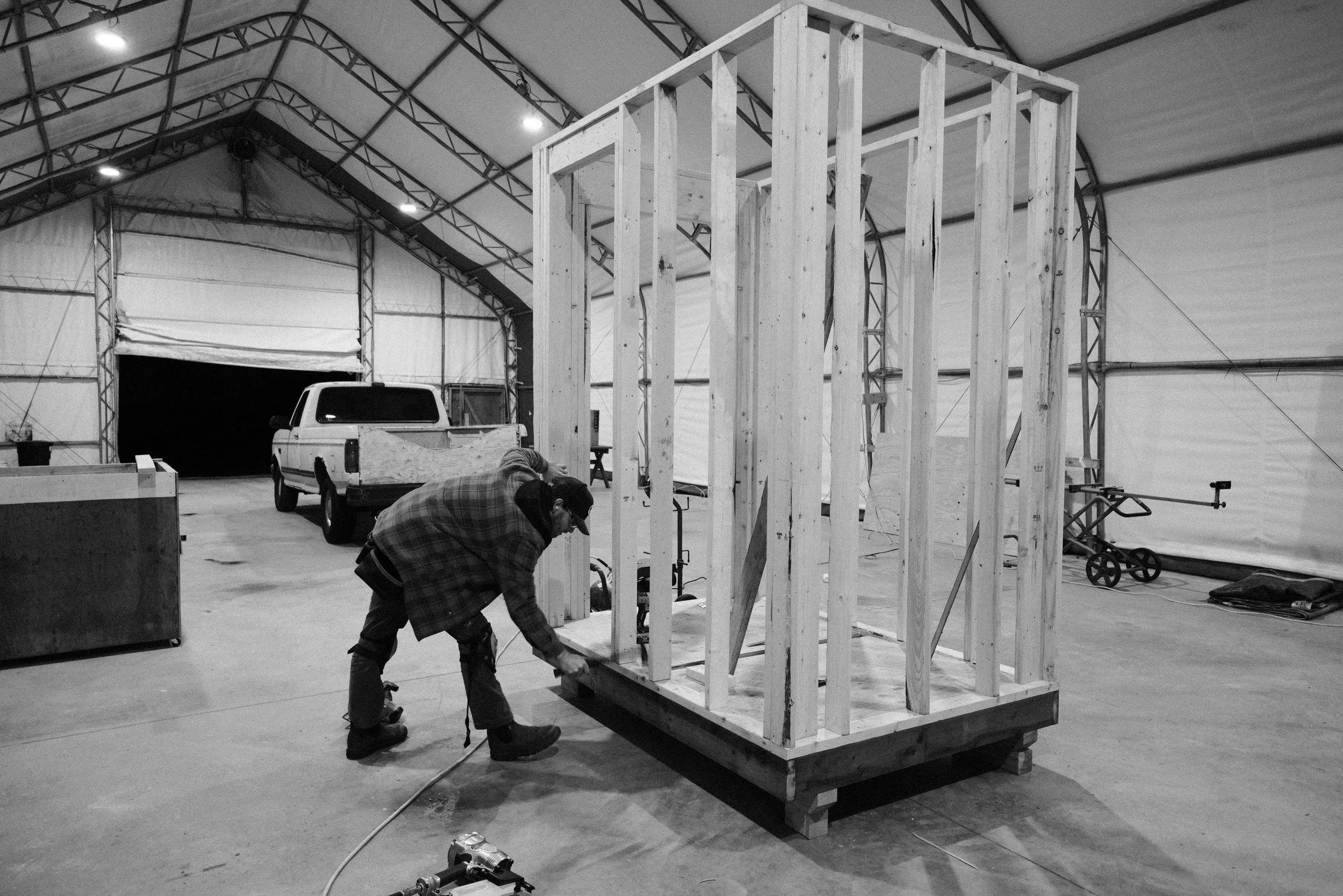 Man building a sauna inside a large warehouse or workshop.