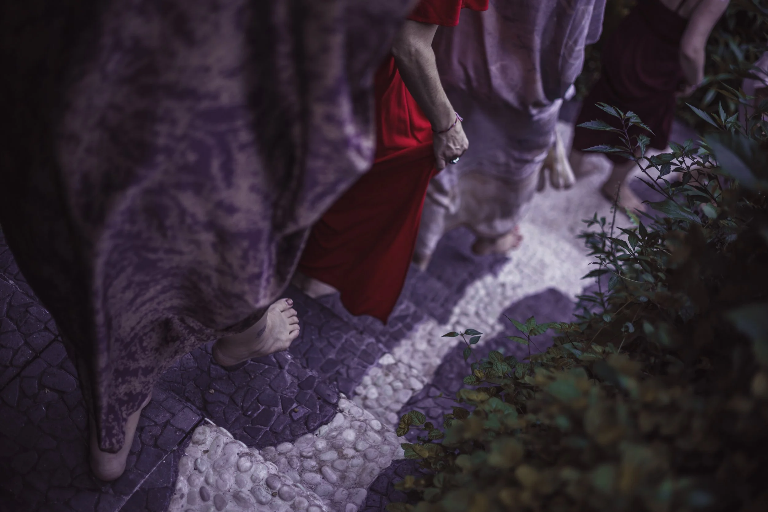 People walking barefoot on a pebble and stone pathway surrounded by greenery.