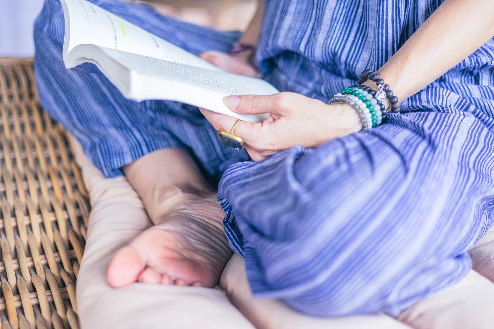 Person wearing striped blue pajamas sitting cross-legged and reading a book.