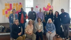 Group of ten people posing together indoors with colorful sticky notes on the wall behind them.