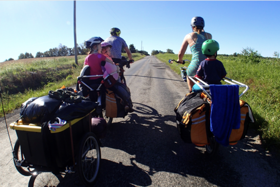 Group of people riding bicycles on a rural road with luggage attached, under a clear blue sky.
