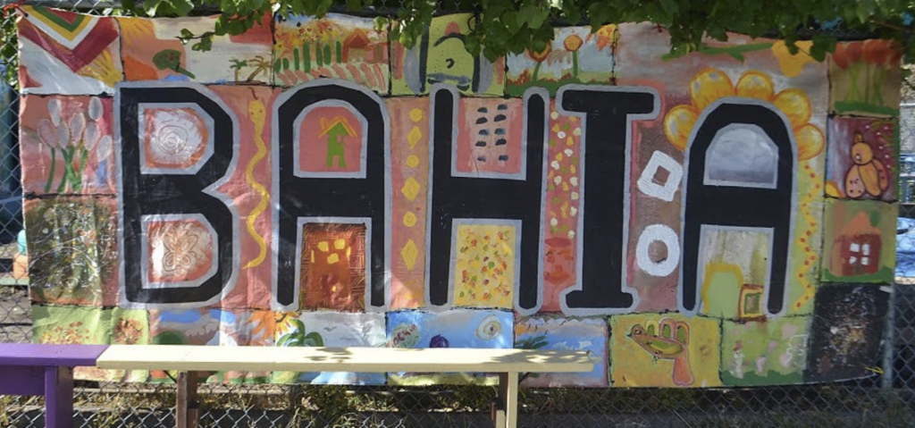 Colorful handmade on fabric or paper banner with the word 'BAHIA' painted on it, decorated with flowers, patterns, and drawings of animals and houses.