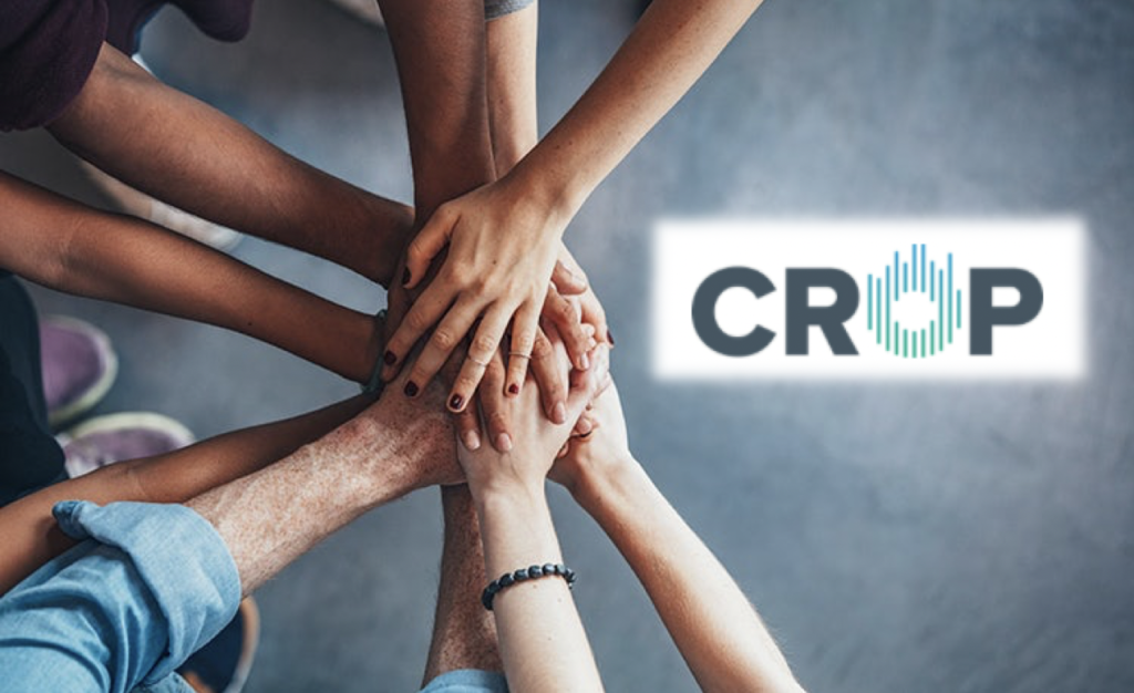 Group of diverse people stacking their hands together in a unity gesture with the word 'CROP' logo to the right.