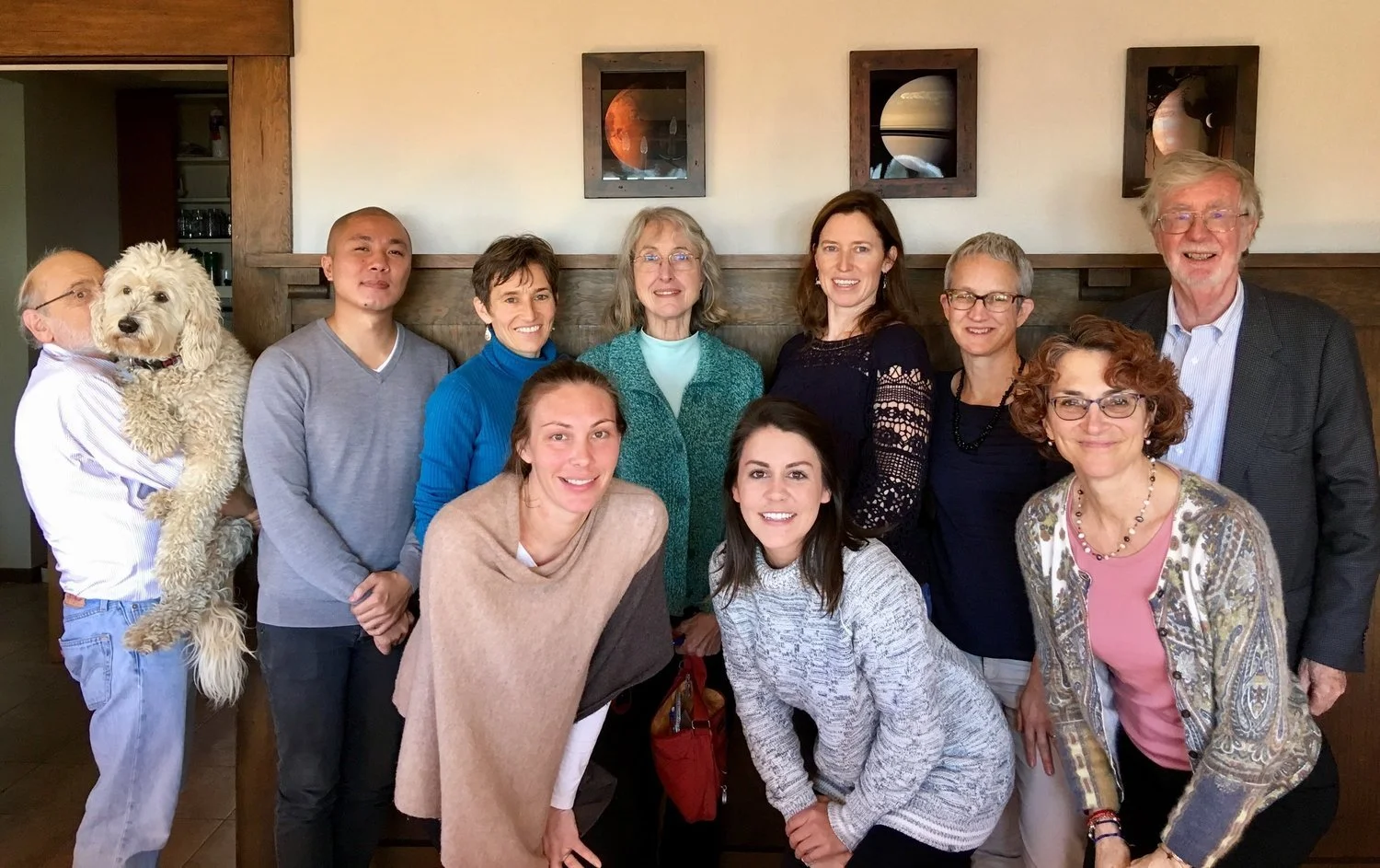 Group of ten people and one dog posing for a photo in a restaurant or cafe, with artwork on the wall behind them.