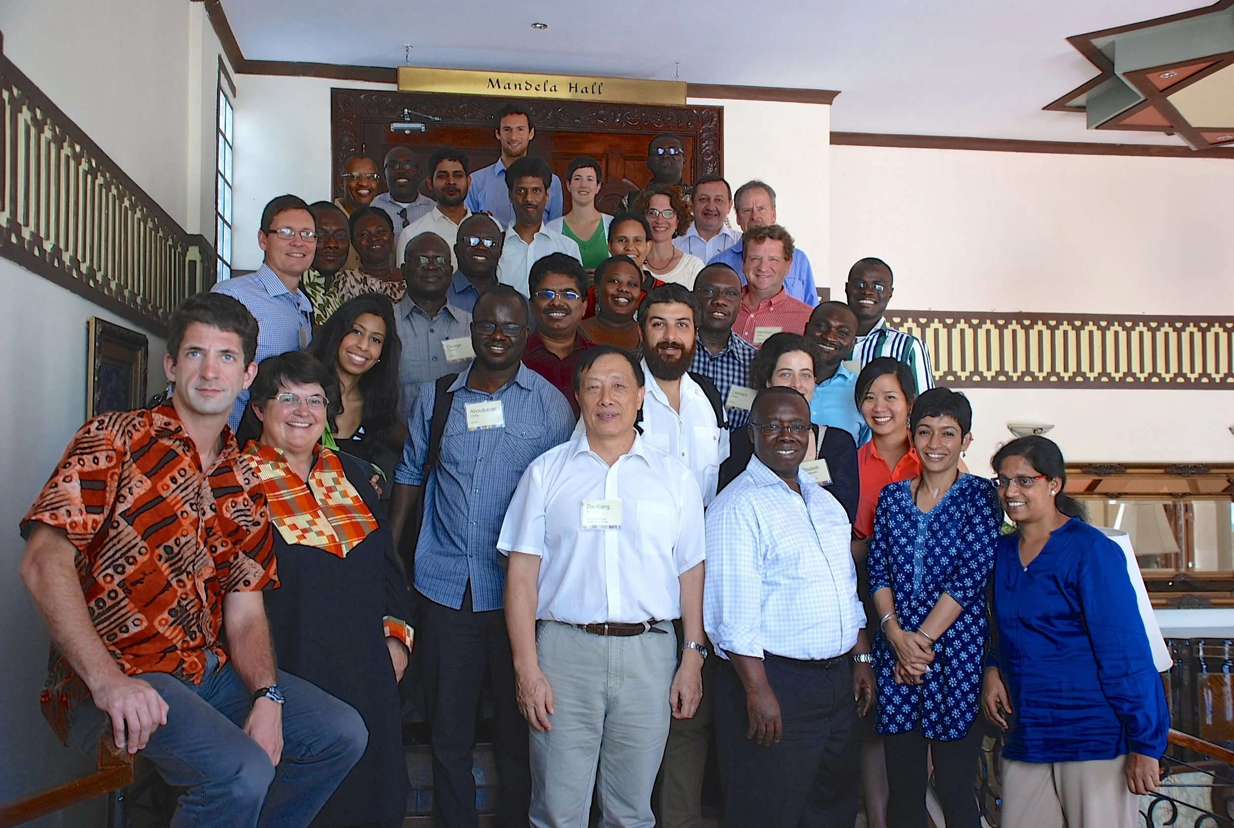 Group of diverse individuals in a conference hall with a sign reading 'Mandela Hall' above the door.