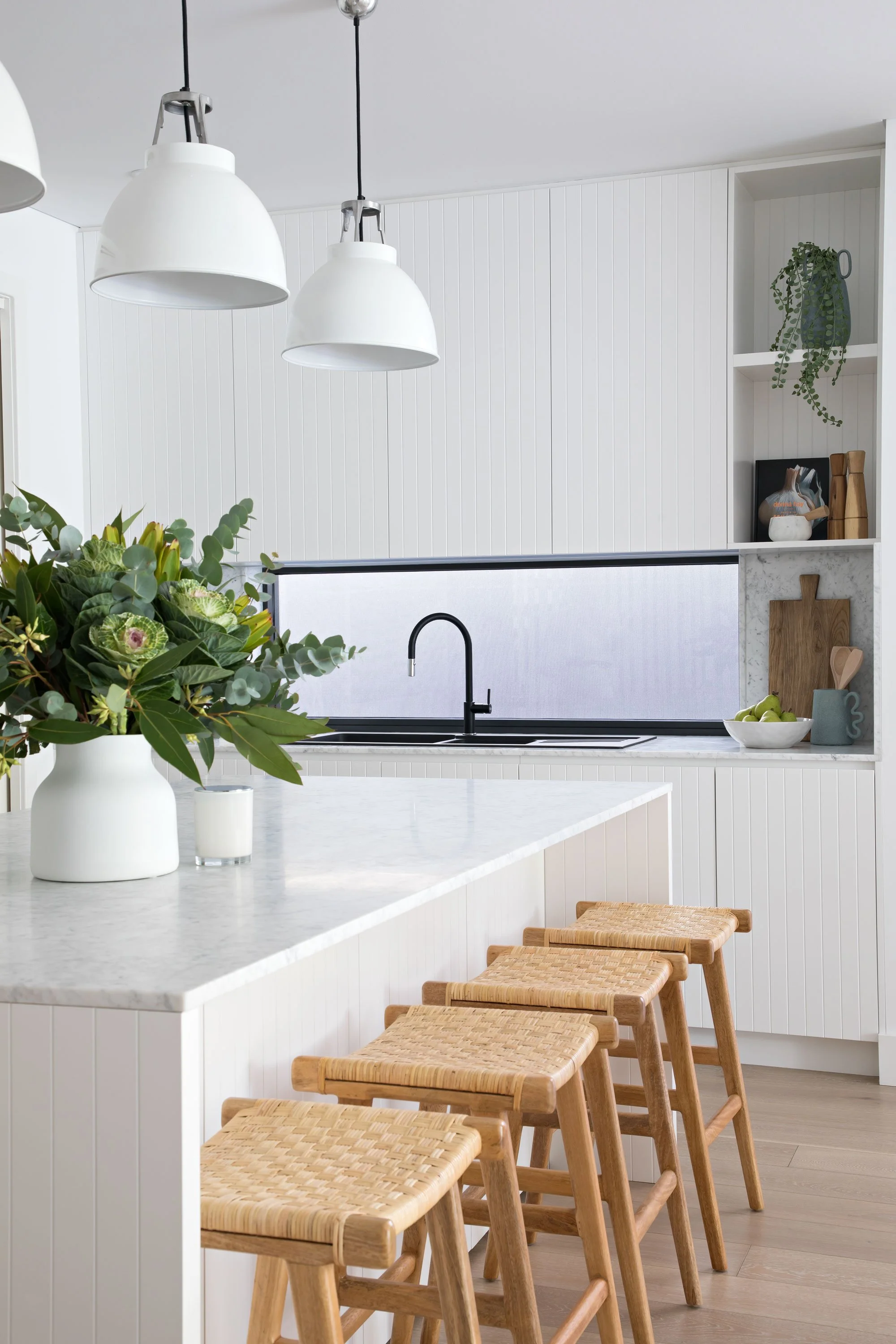 White kitchen island woven topped stools 3 white pendant lights vase flowers