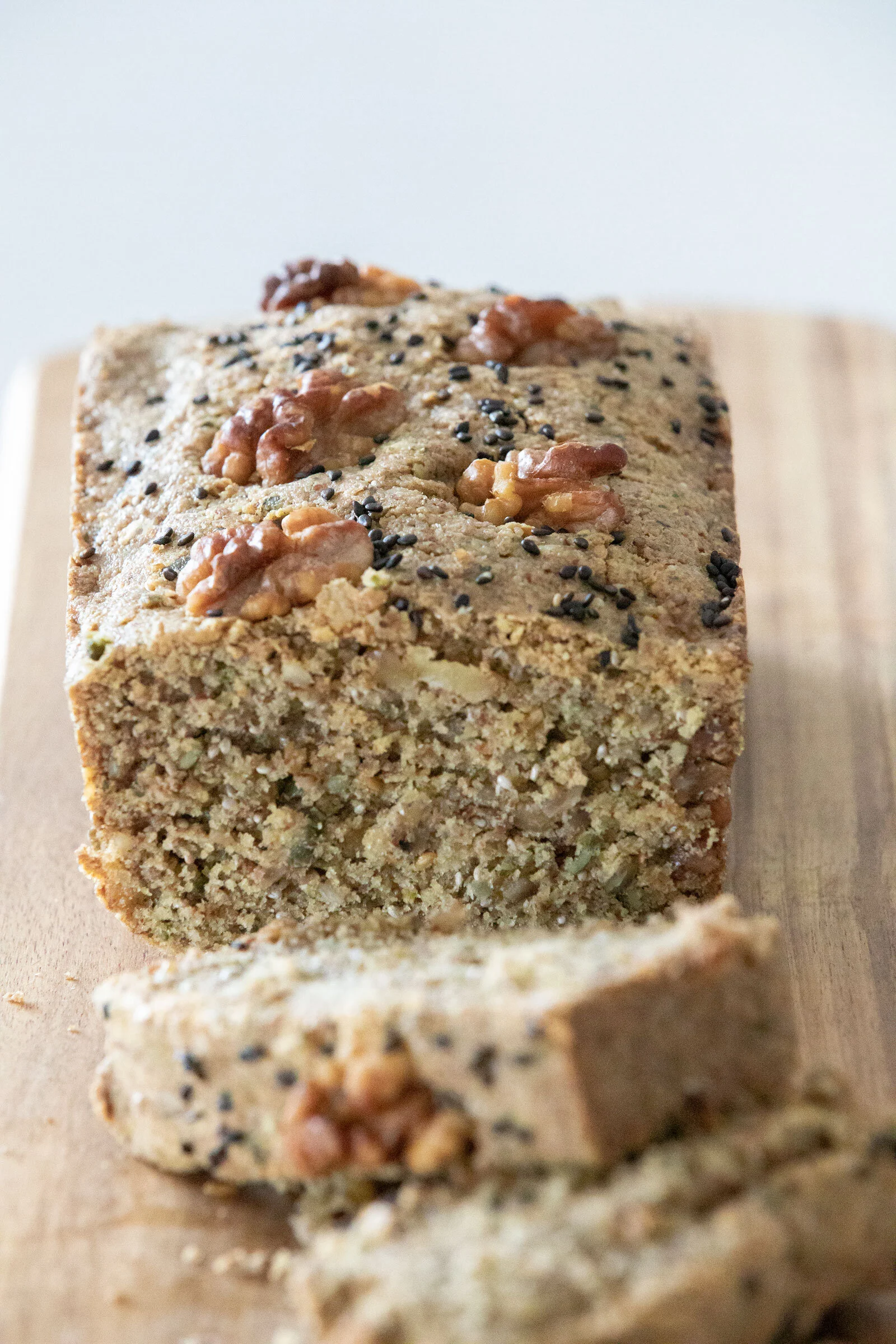 Close-up of rectangular multigrain bread with nuts and seeds on top, placed on a light wooden surface.