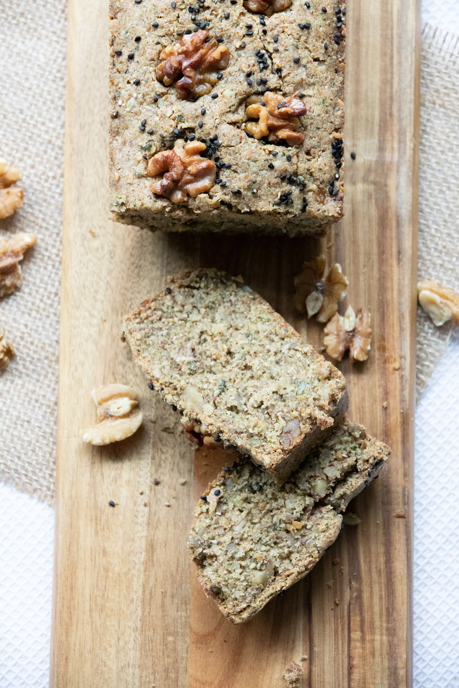 Four slices of nut and seed loaf bread topped with walnuts and black sesame seeds on a wooden serving board.