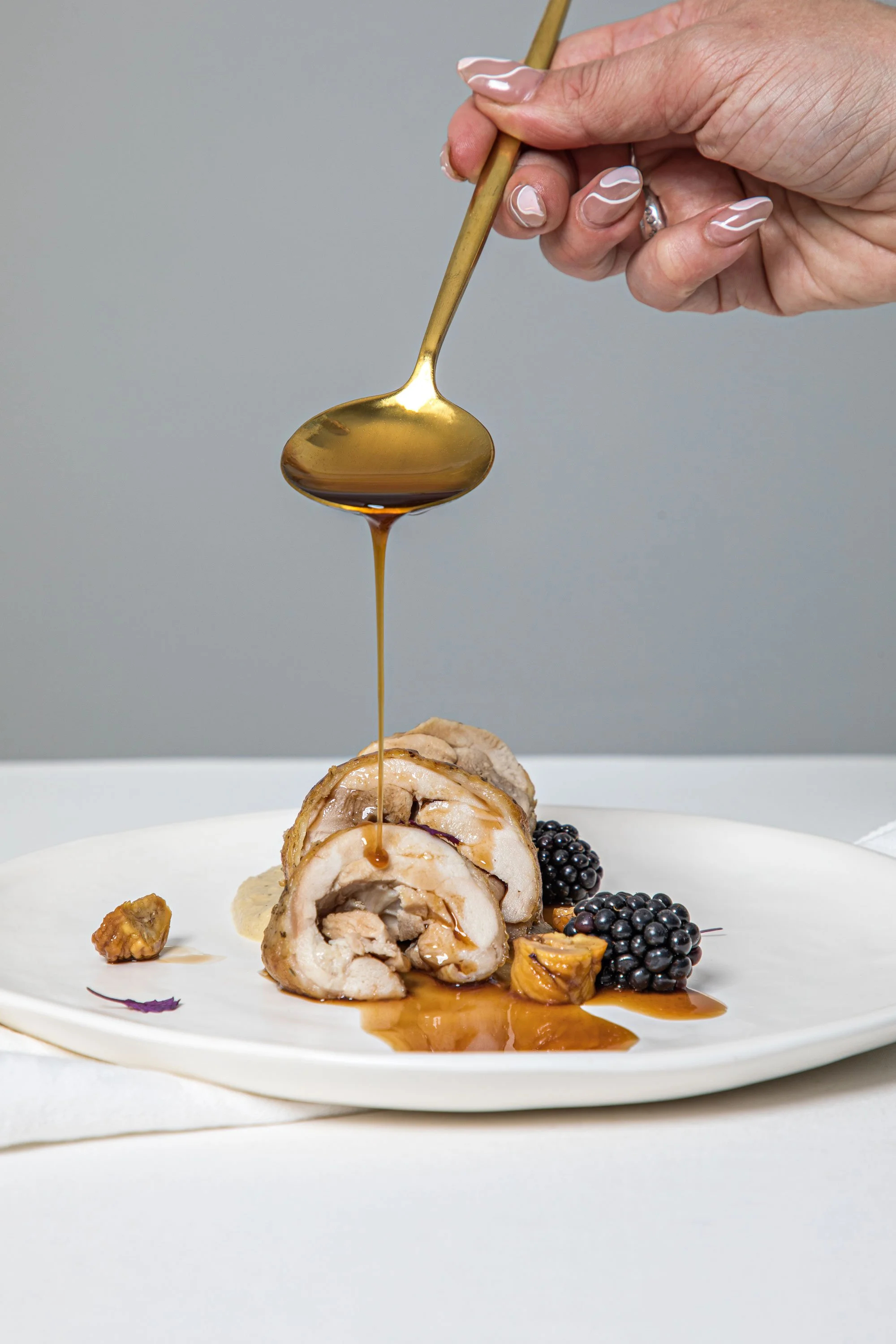 Sliced rolled chicken breast stuffed with feta and spinach, topped with balsamic glaze, served with blackberries, figs, and a drizzle of sauce on a white plate.
