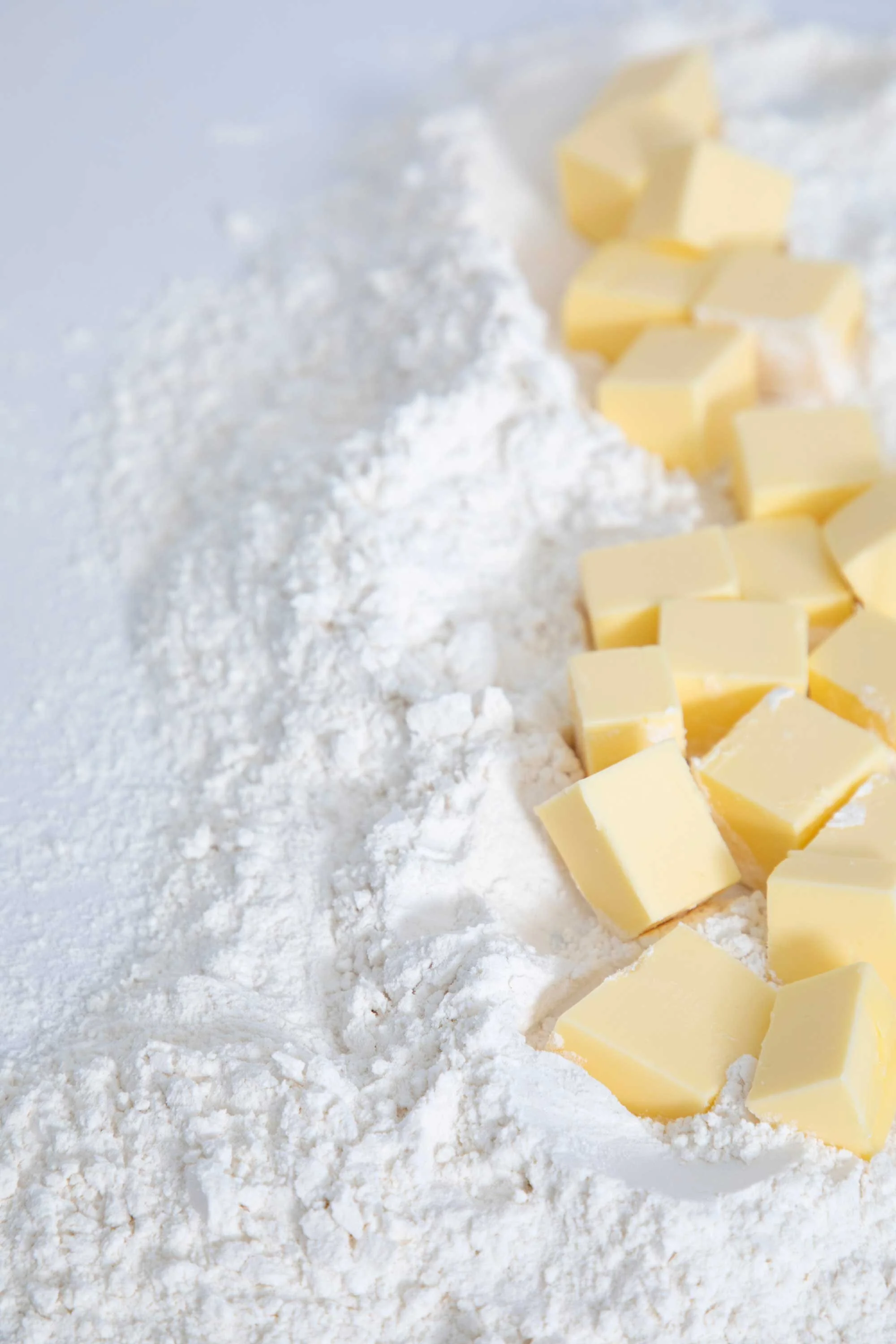 Slices of butter arranged on a bed of flour along with a pile of flour on the left side of the image.