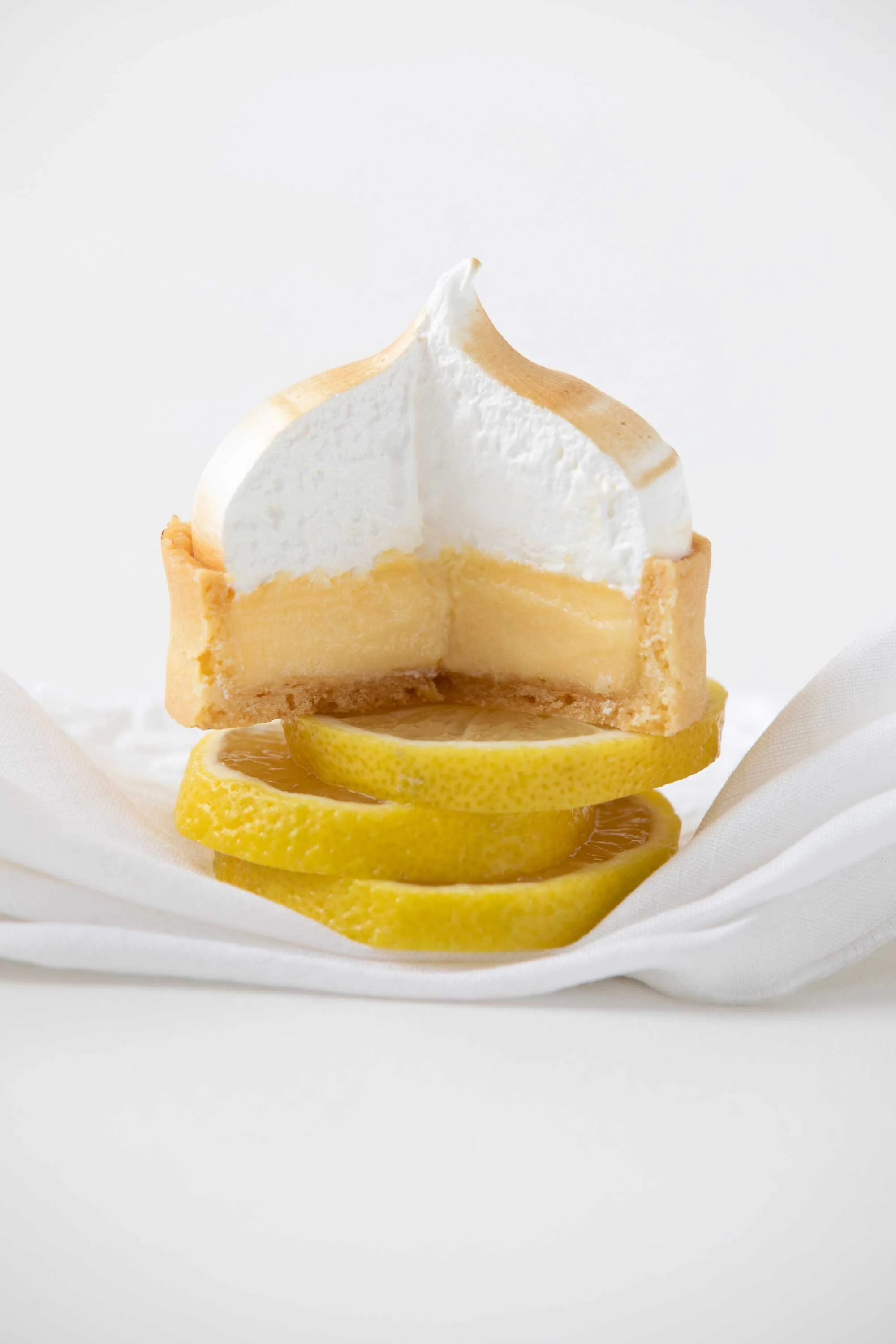 A lemon tart topped with whipped cream, placed on a lemon slice and white fabric.