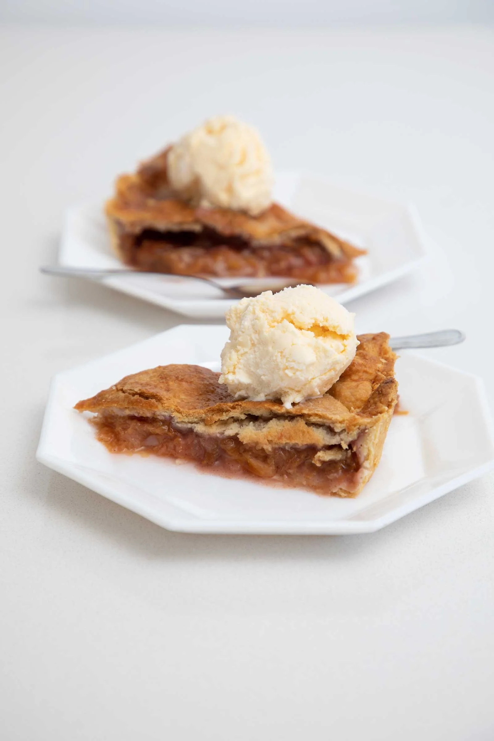 A slice of cherry pie with a scoop of vanilla ice cream on top, served on a white plate.