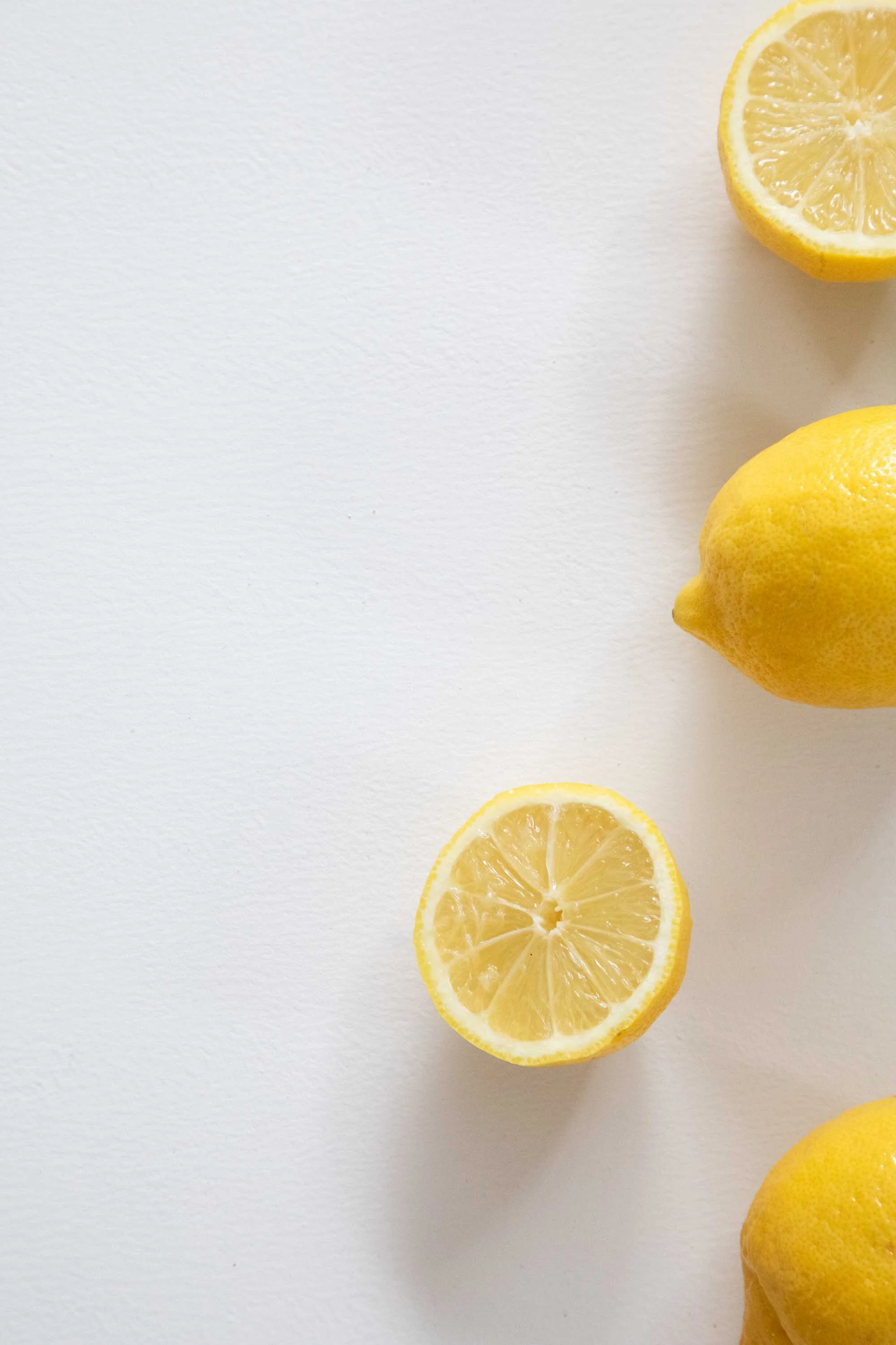Several halved lemons placed on a white surface, with some whole lemons nearby.