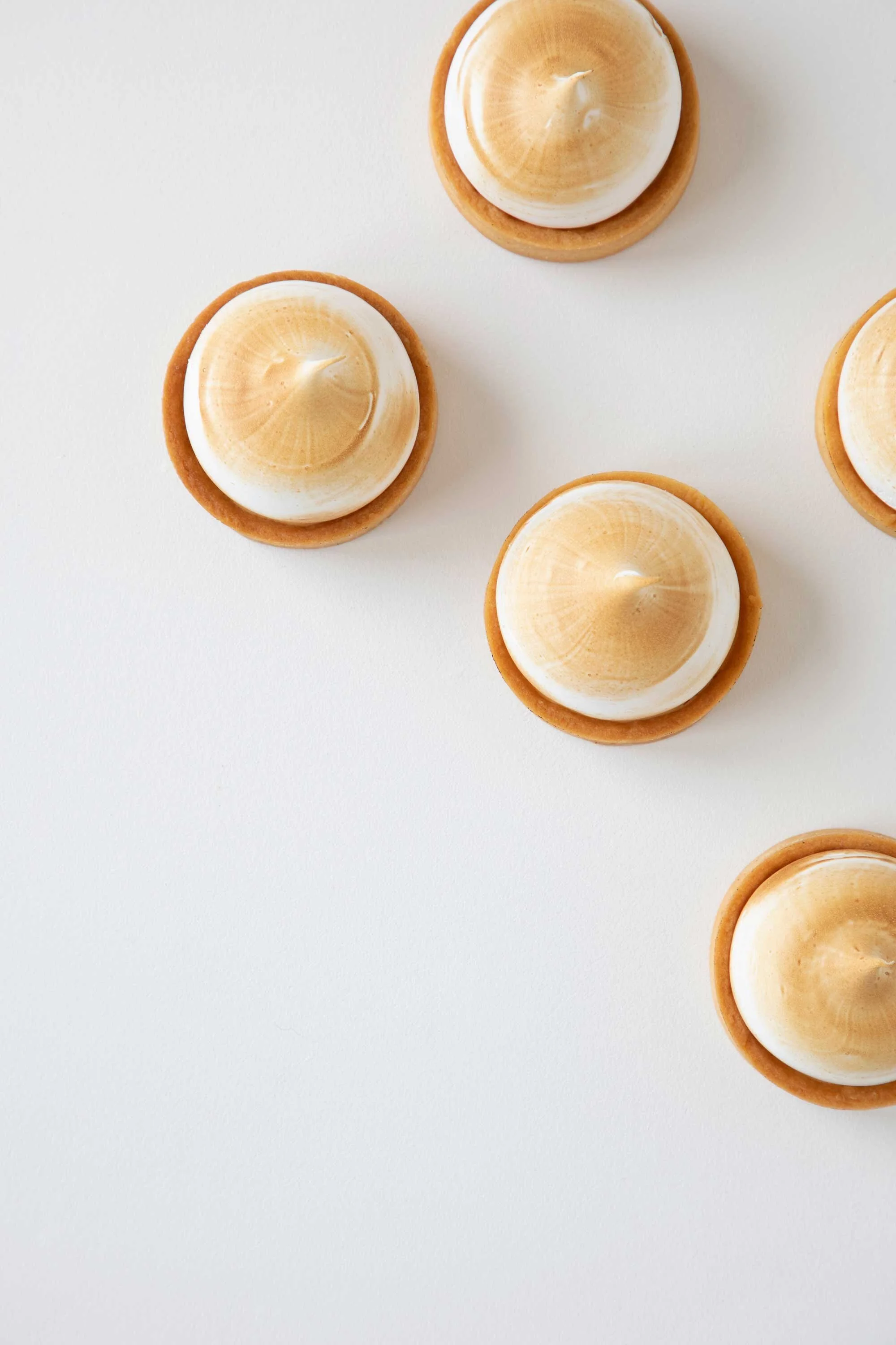 Top view of three tarts with cream and caramel topping on a white surface, with empty space on the bottom and left.