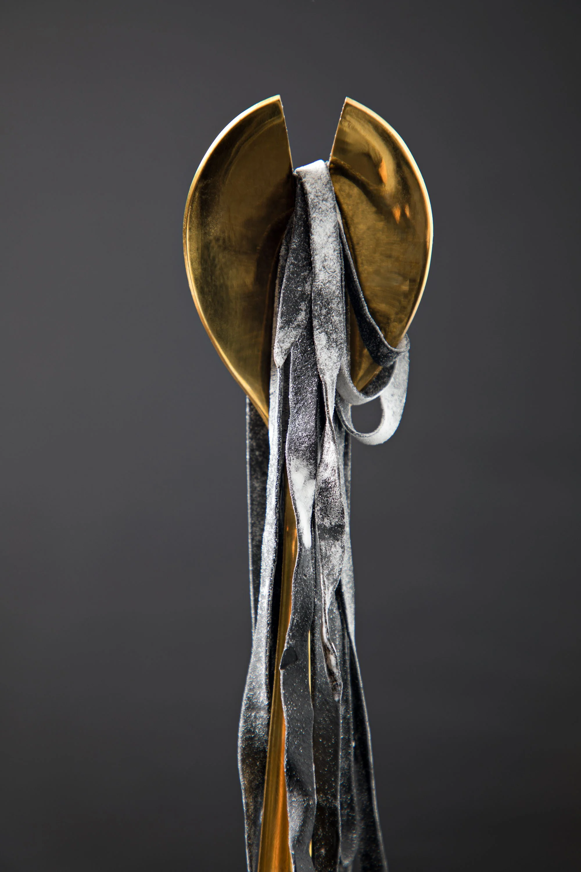 Close-up of a pair of vintage metal tongs with a black, powdery substance on the handles and some gold-colored liquid or material dripping from the tip.