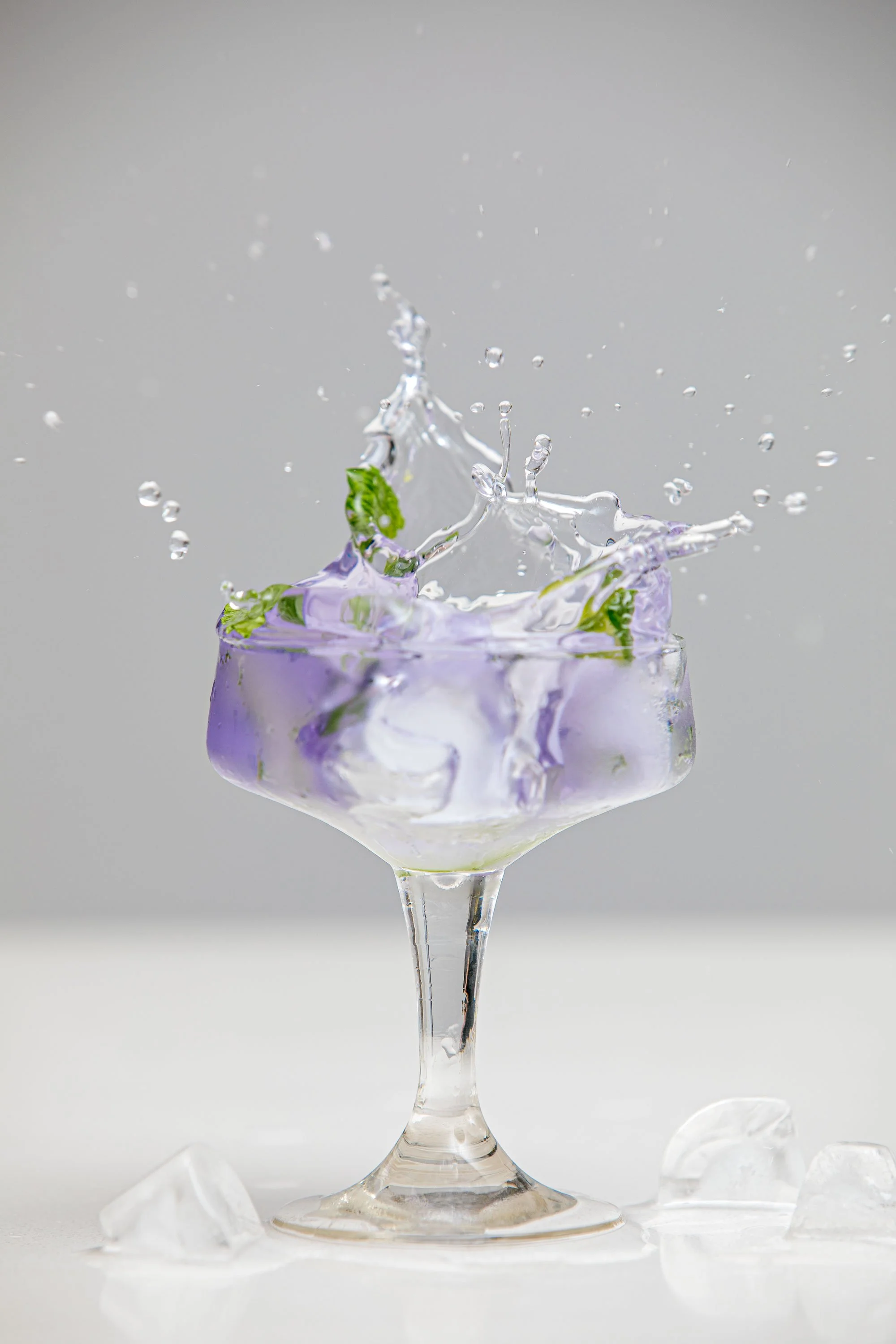 A glass of water with ice and mint leaves, with water splashing out and ice cubes on the surface.