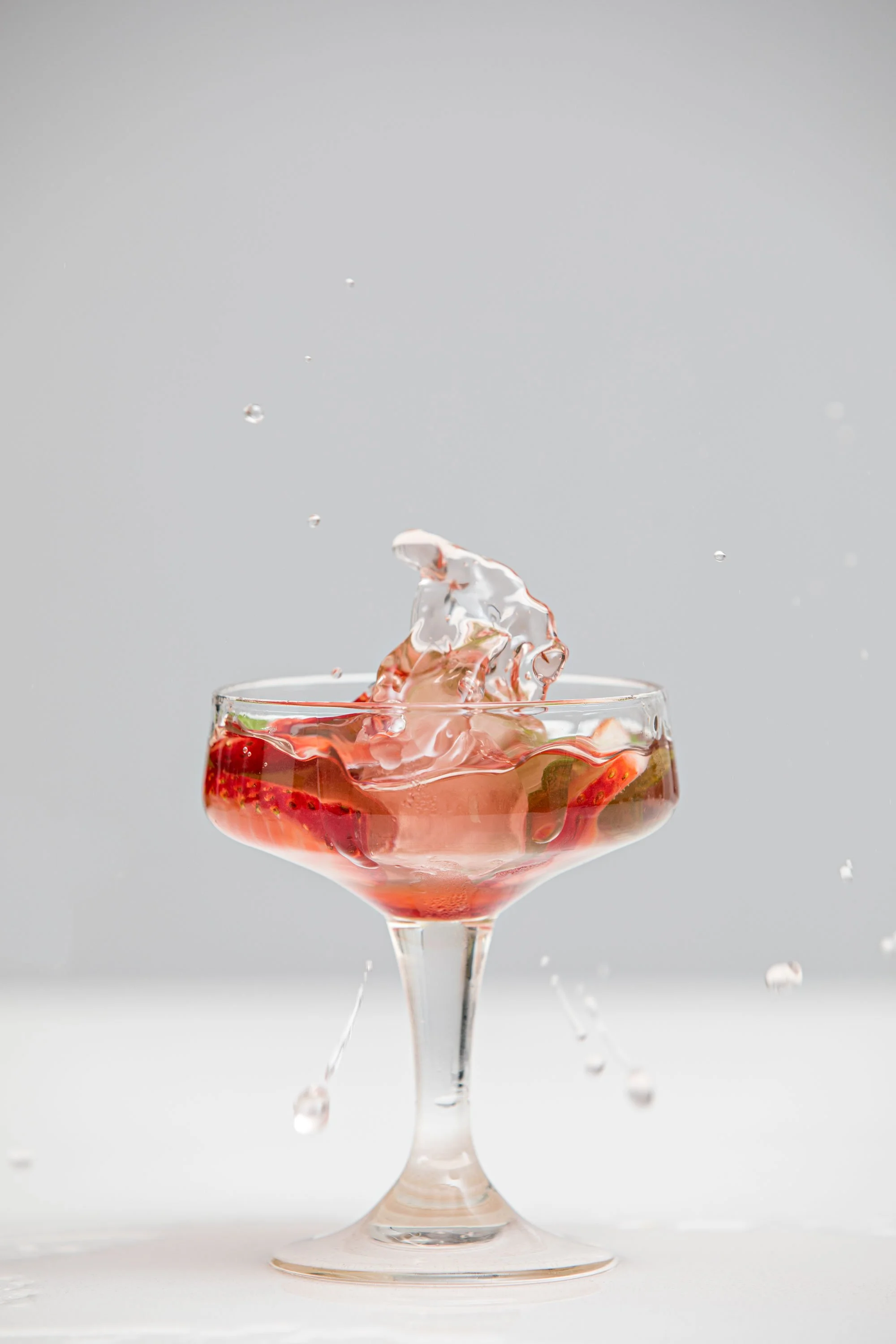 A glass of strawberry juice with ice and strawberry slices, captured mid-splash with water droplets in the air.