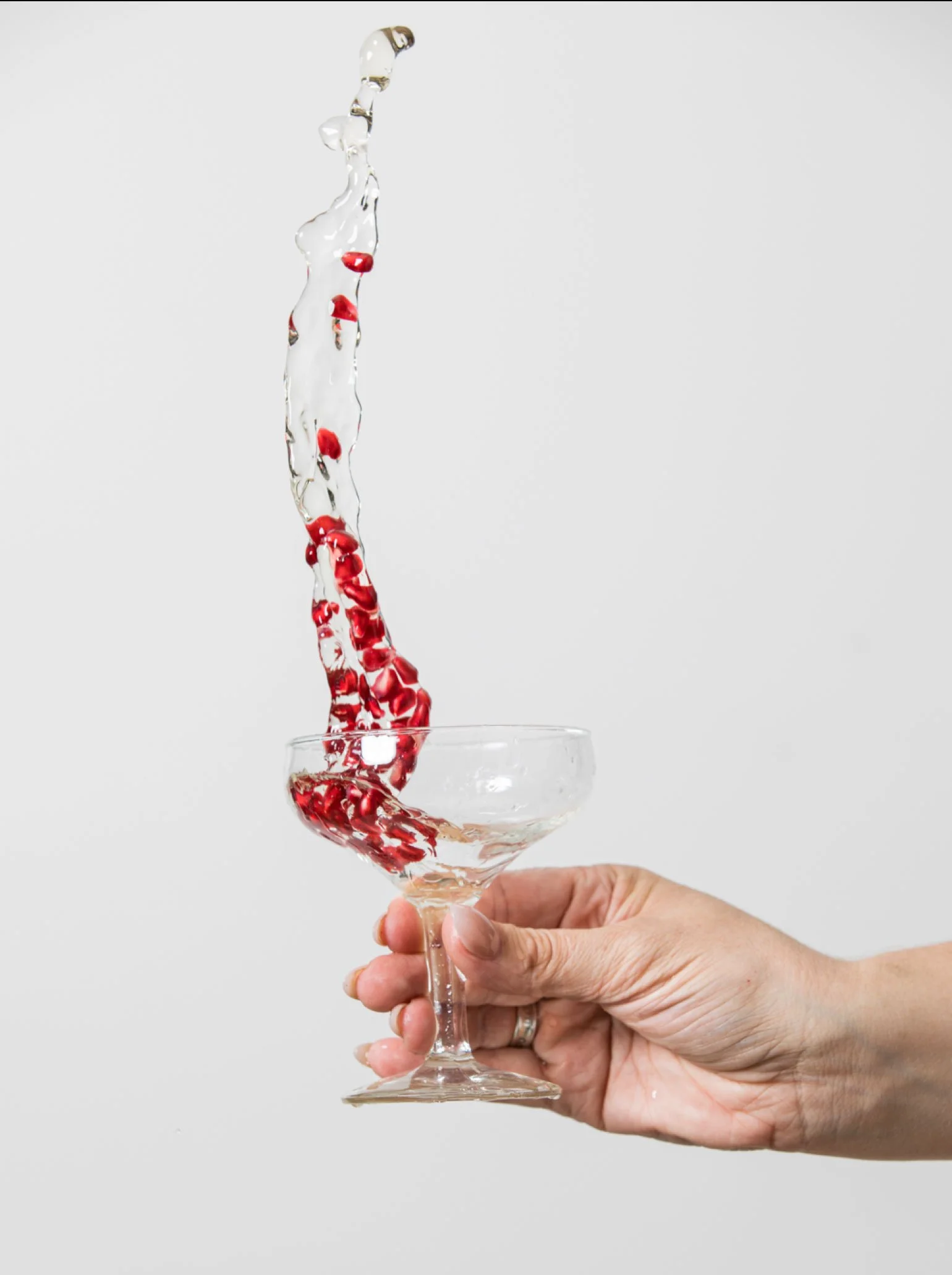 A hand holding a glass of water with pomegranate seeds, swishing it around and creating a splash.
