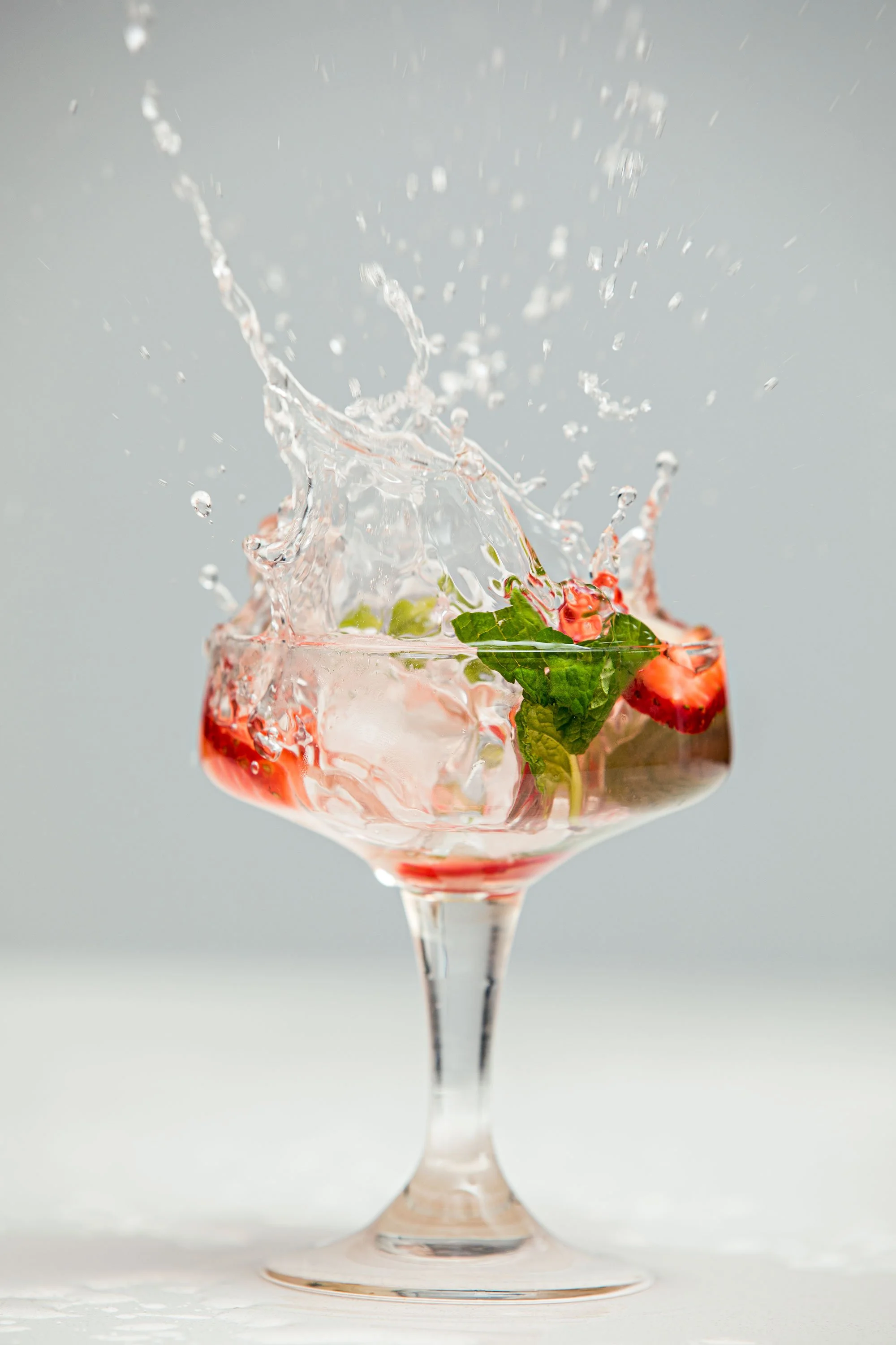 Strawberries, mint leaves, and ice cubes in a glass with water splashing out.