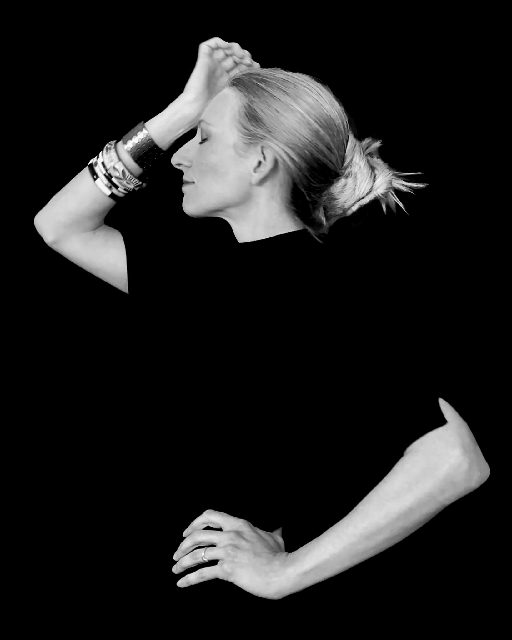 Black and white photo of a woman with her hands on her forehead, eyes closed, and a peaceful expression, wearing multiple bracelets on her wrist.