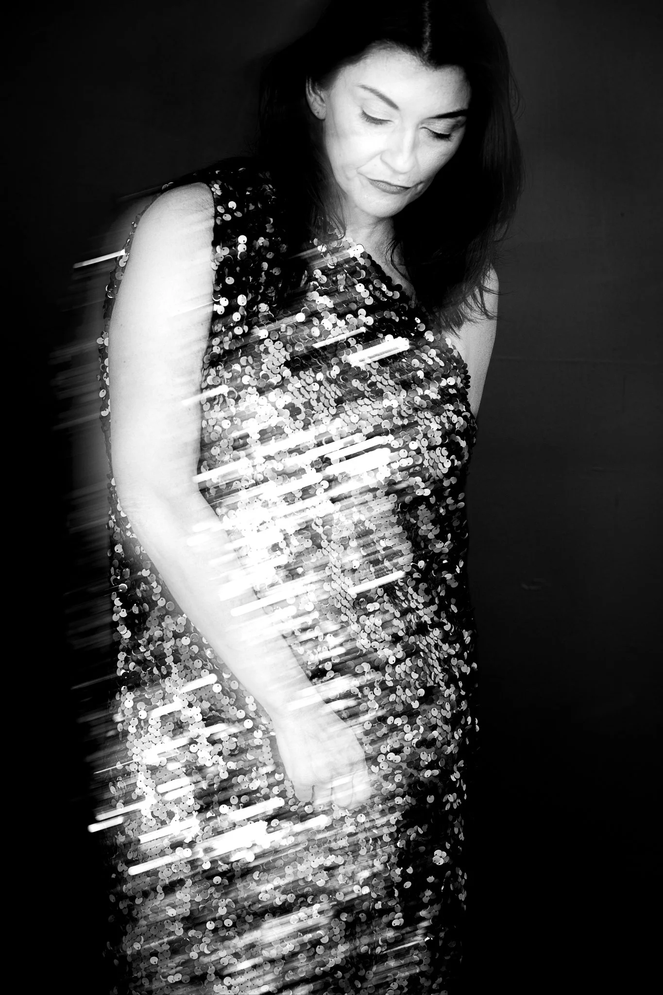 Black and white portrait of a woman with dark hair wearing a sequined dress, looking downward with closed eyes.