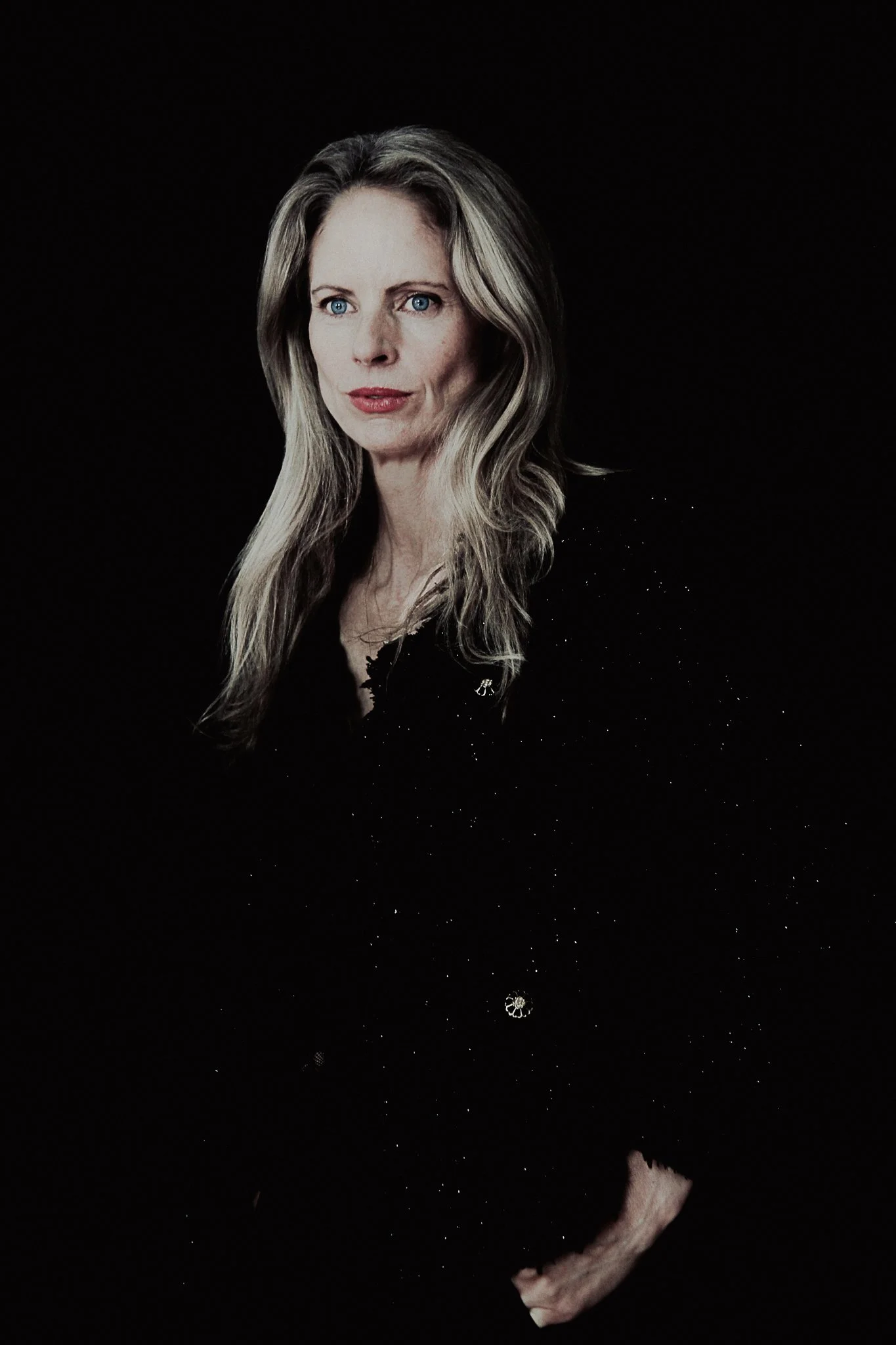 A woman with blonde hair in a black outfit, set against a black backdrop with small sparkling dots and a faint crescent moon at the bottom.
