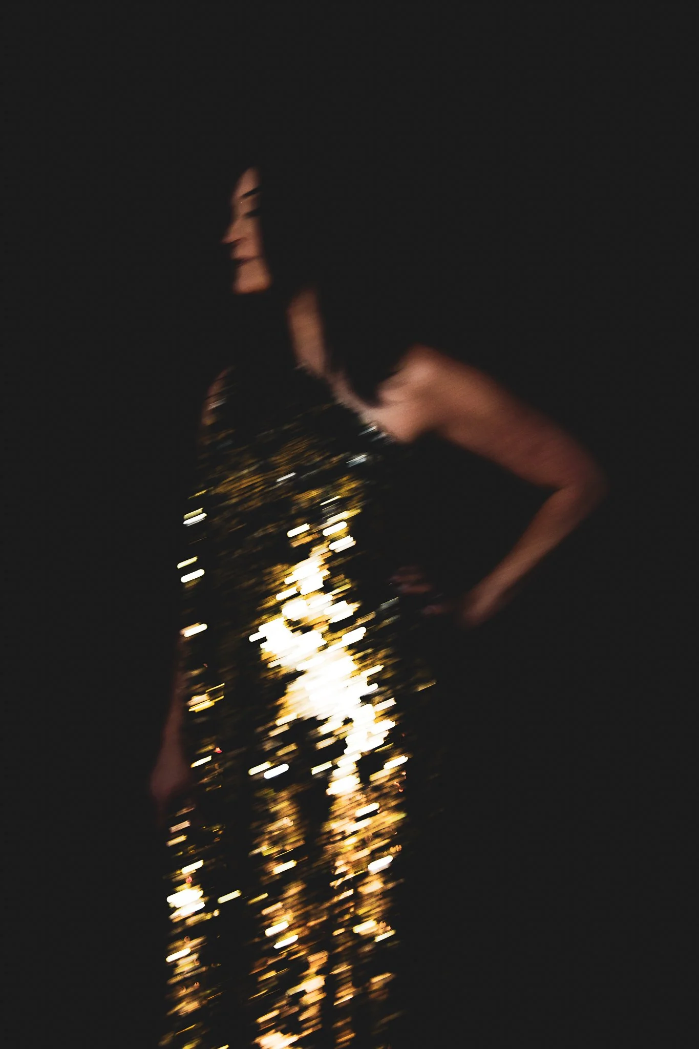 Person wearing a black dress with gold sequins, standing in a dark environment, with the dress sparkling in the light.