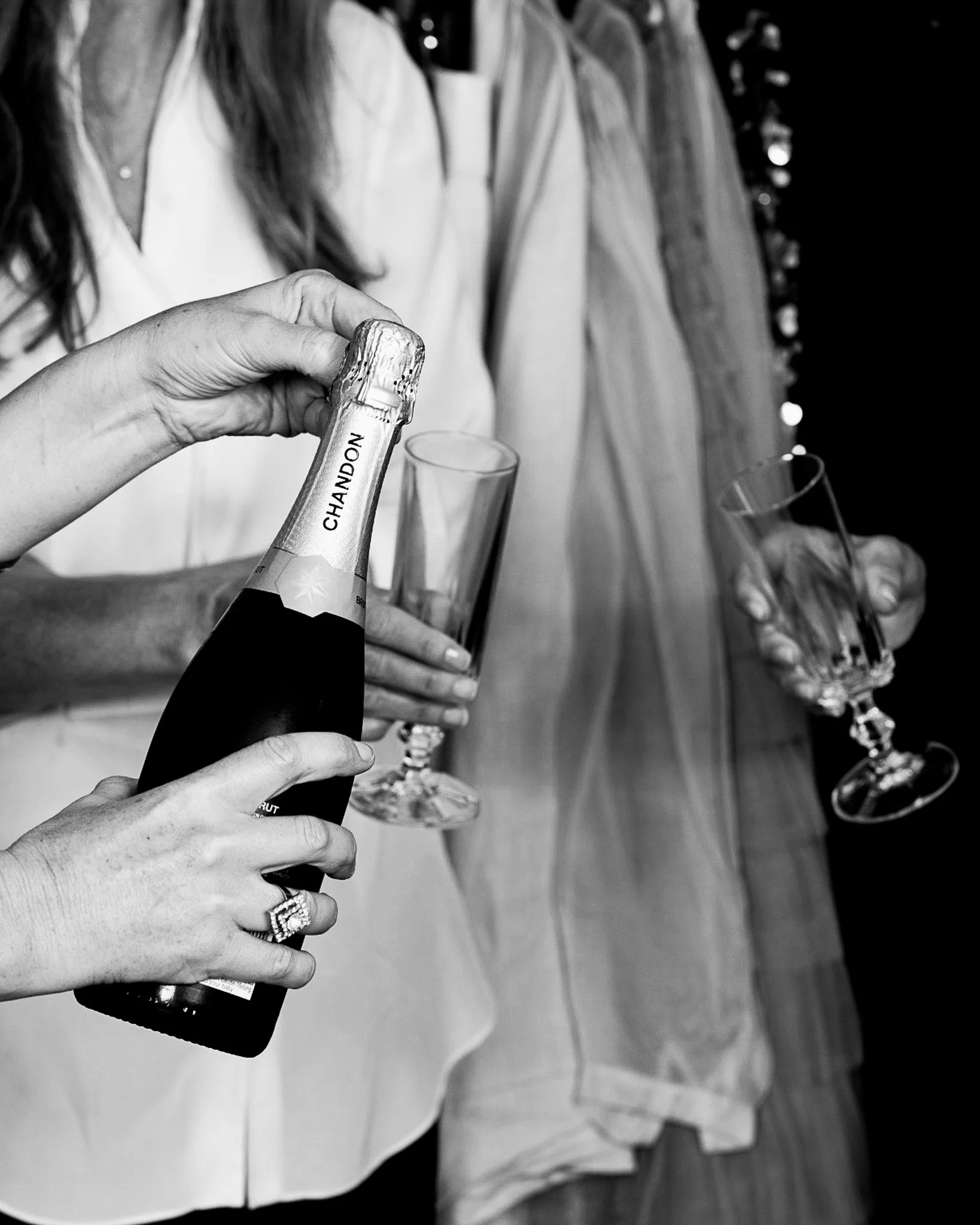 Close-up of a person holding a bottle of champagne with a 'CHANDON' label, with several empty champagne glasses in the background.