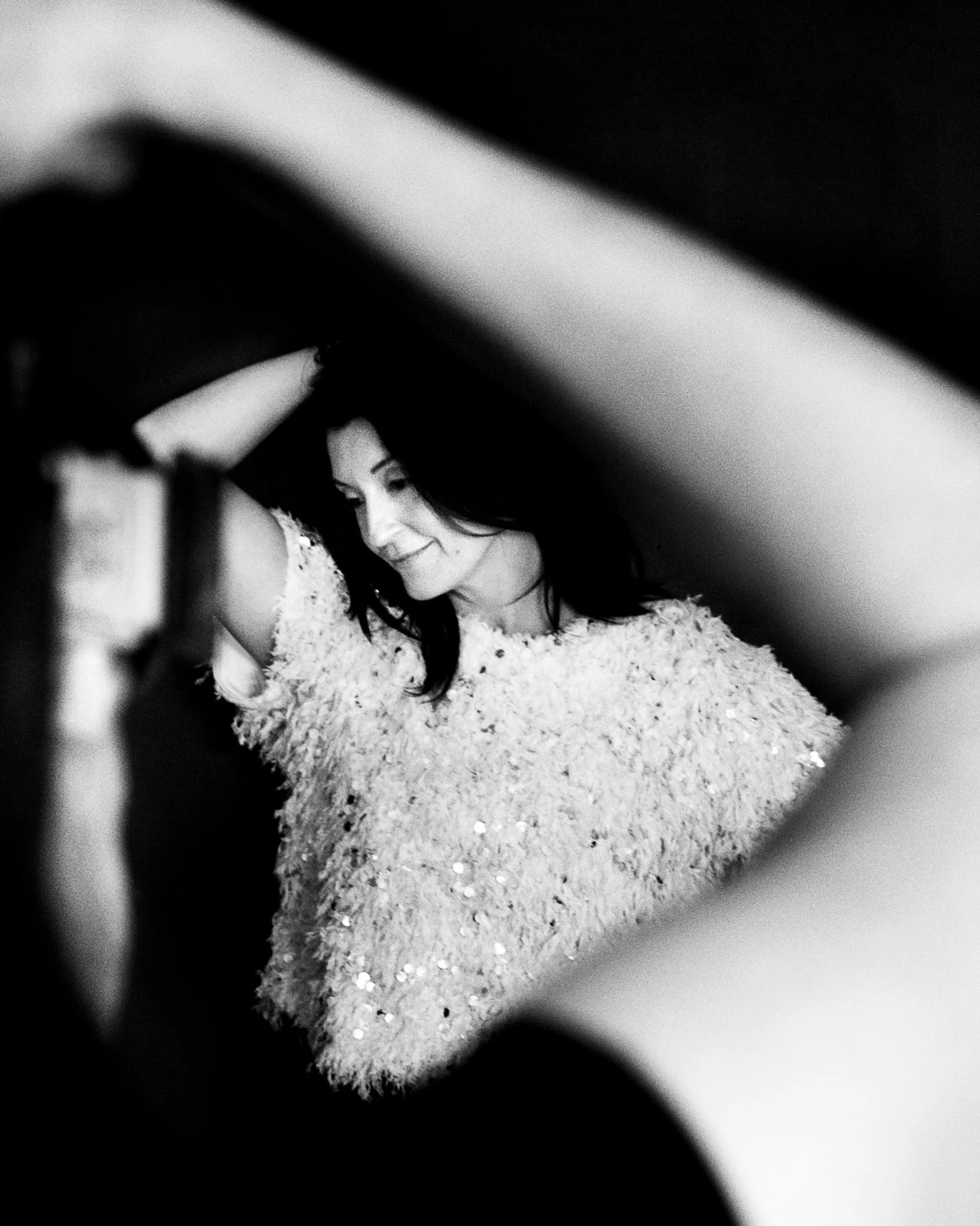 A woman with dark hair smiling, wearing a floral dress, captured through a blurred, circular frame with a black and white filter.
