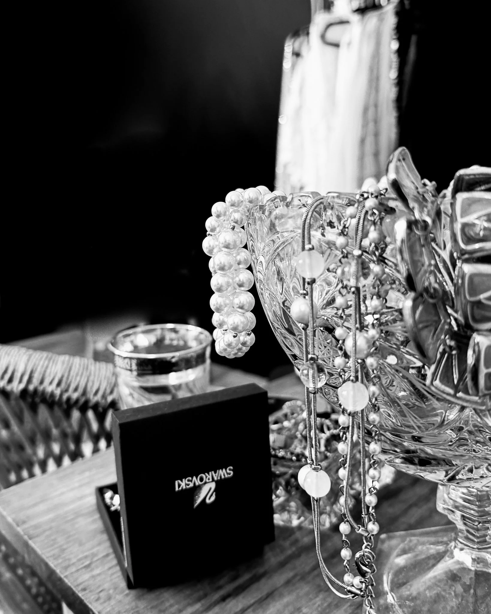 Close-up black-and-white photo of jewelry including pearl necklaces, bracelets, and other accessories displayed in a glass bowl.