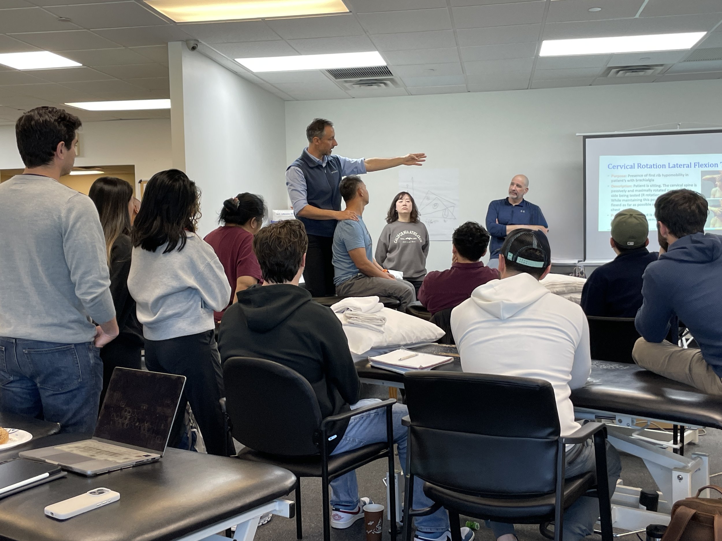 Instructor teaching manual therapy techniques to a class of physical therapy learners in a hands-on workshop.