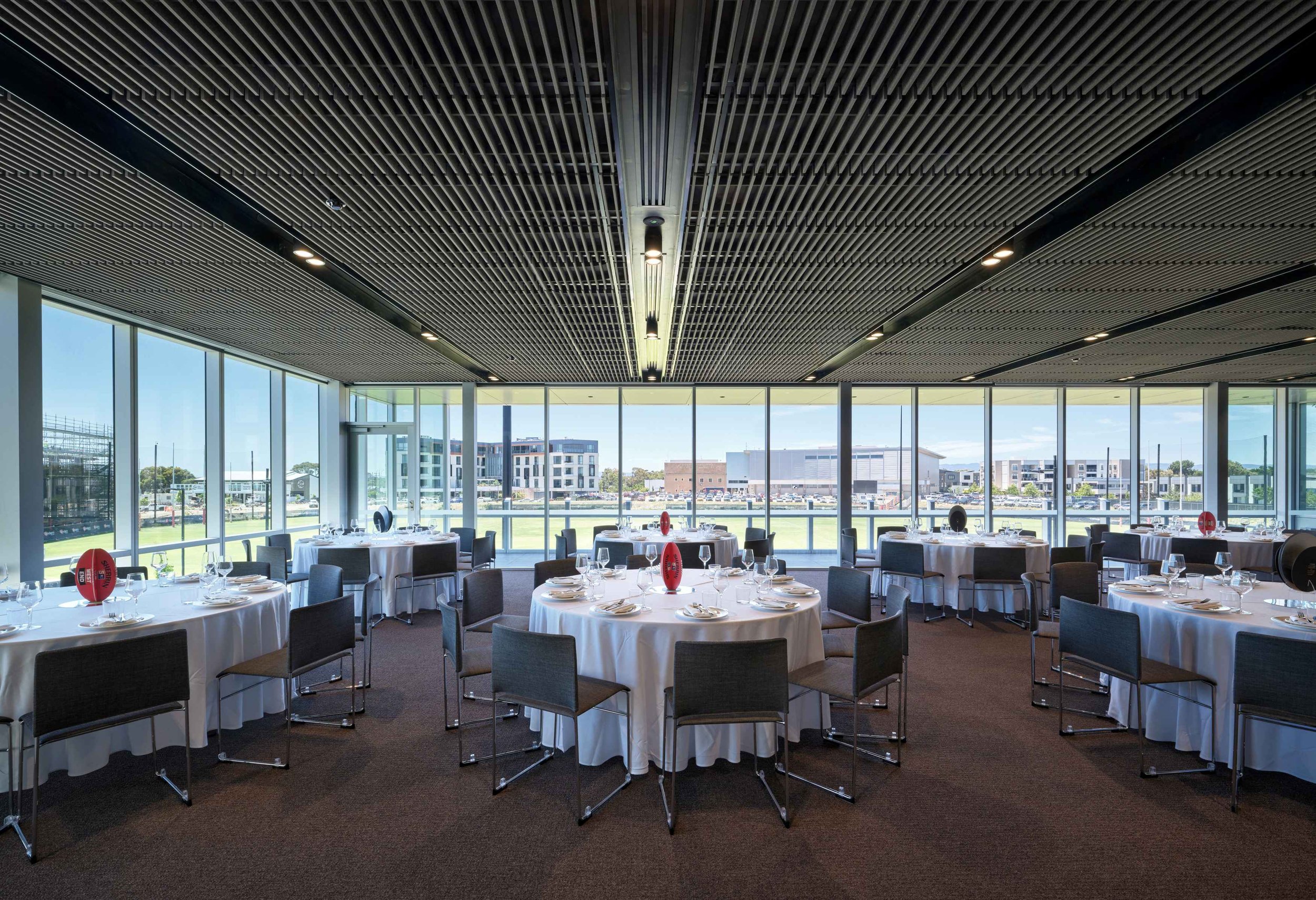 Modern conference room with round tables and chairs, large windows, and a few people sitting and standing.