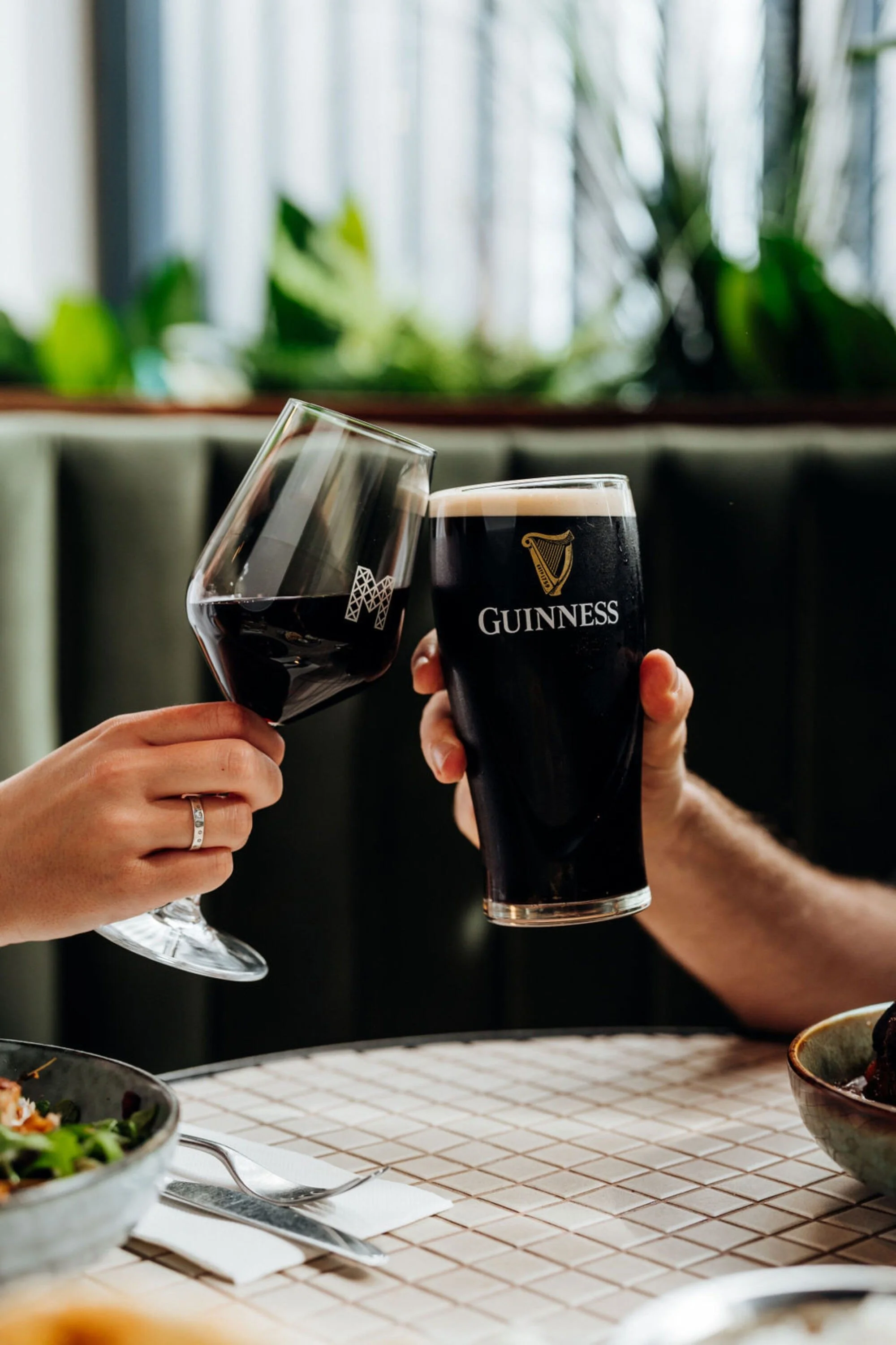 A woman and a man raising glasses of red wine and Guinness beer in a toast at a dining table.