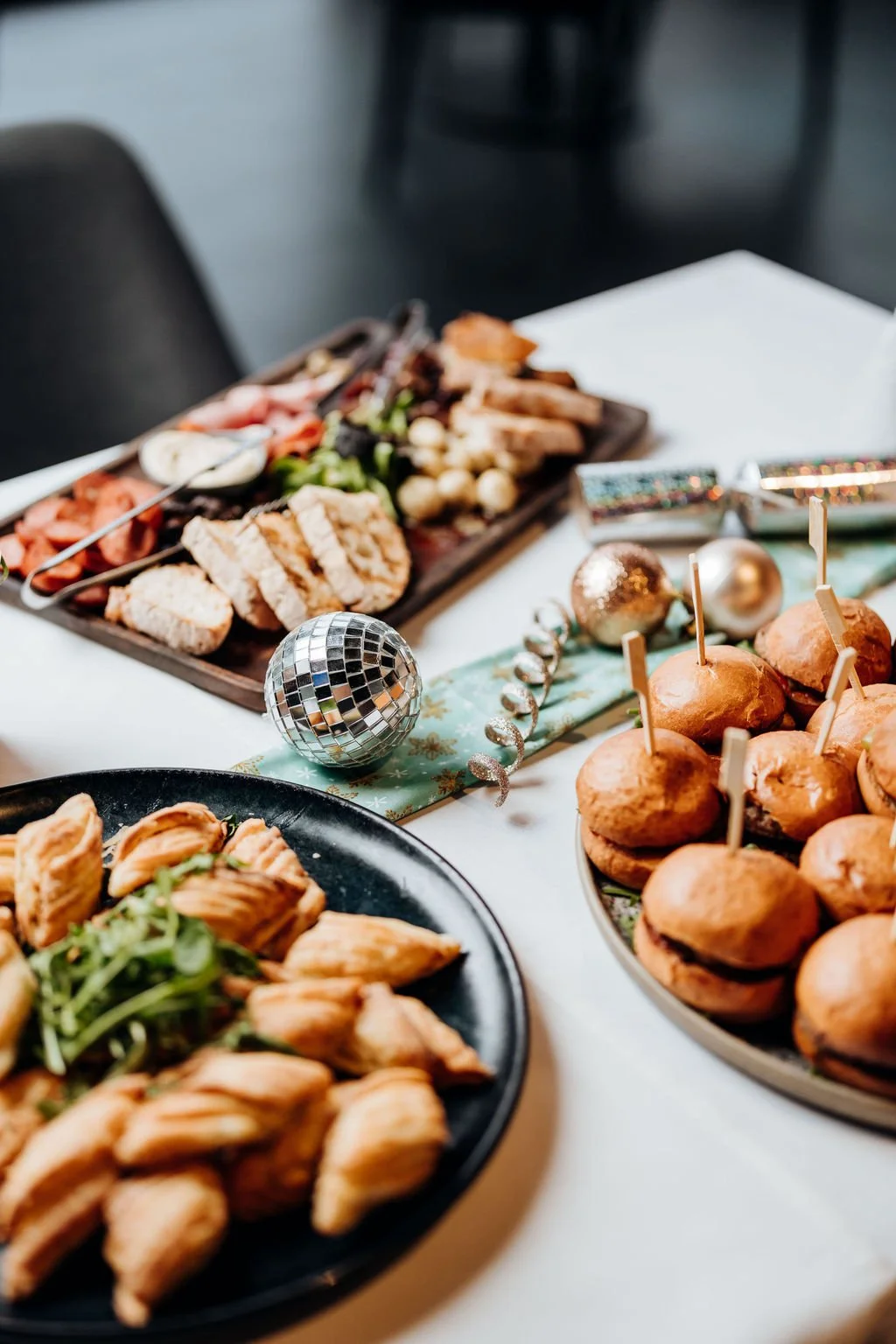 Party table with assorted snacks, sliders, and Christmas decorations including a disco ball and ornaments.