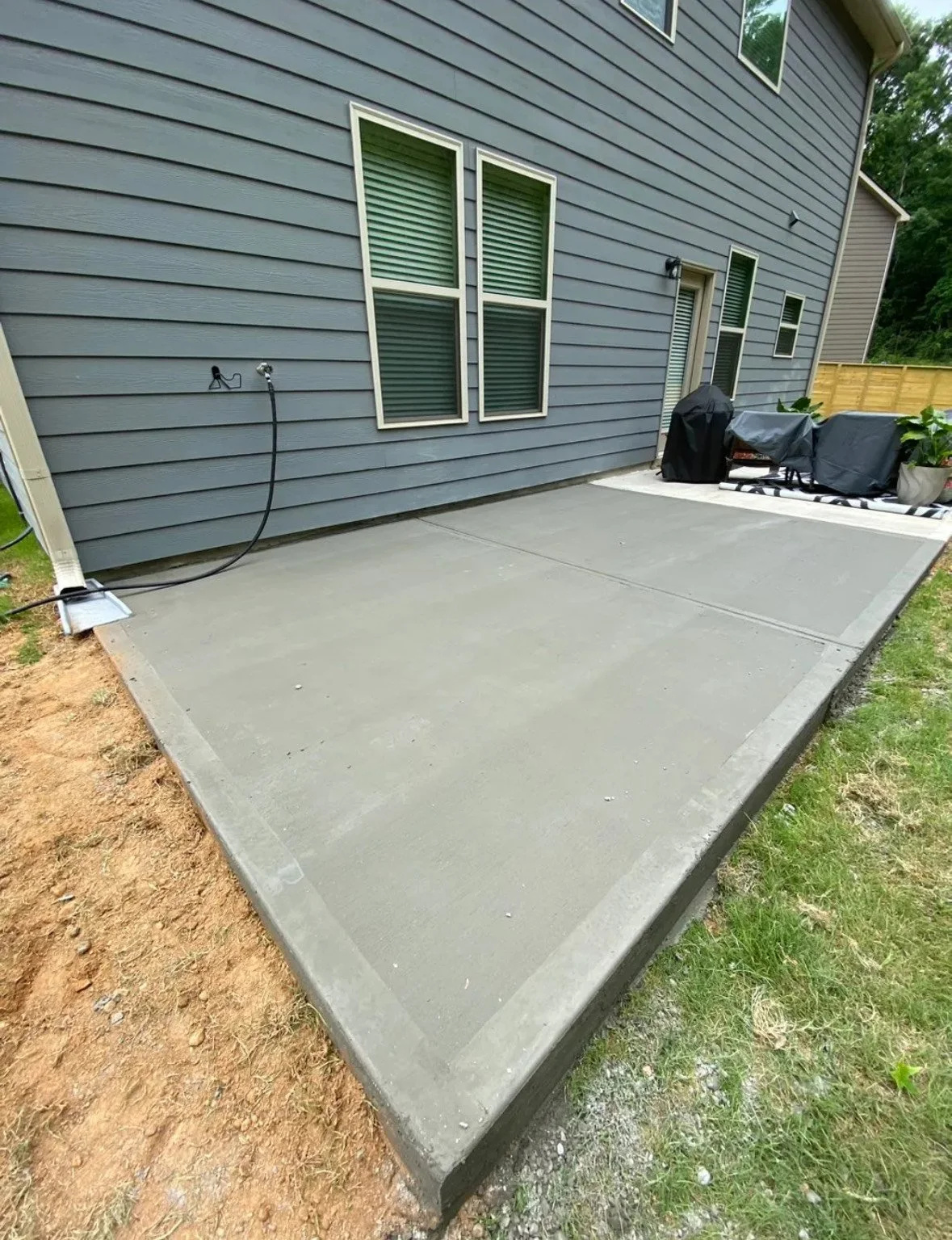 Freshly poured concrete patio in the backyard of a blue house with windows.