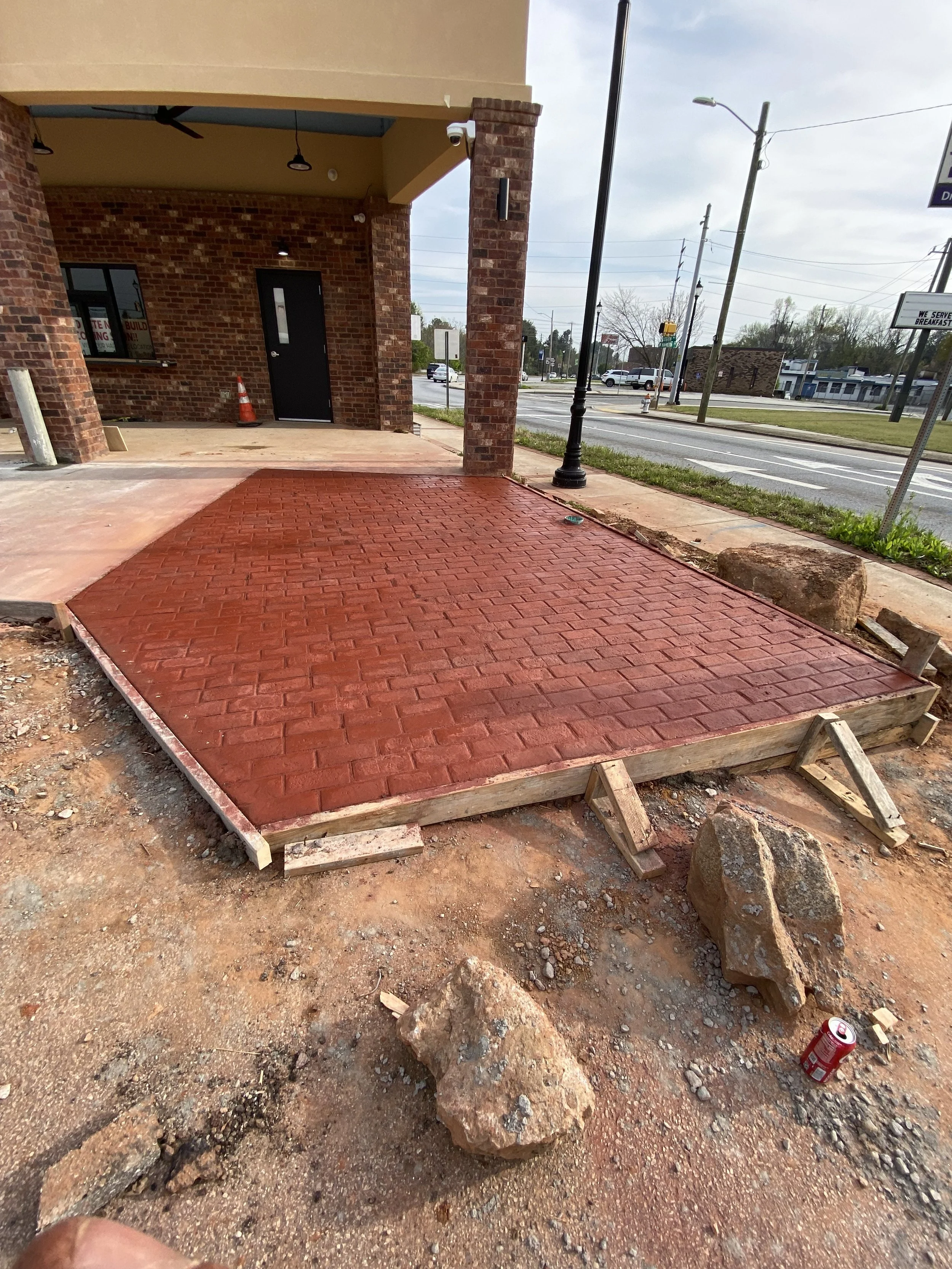Freshly laid red brick sidewalk in front of a brick building under construction, with construction materials and rocks on the ground.