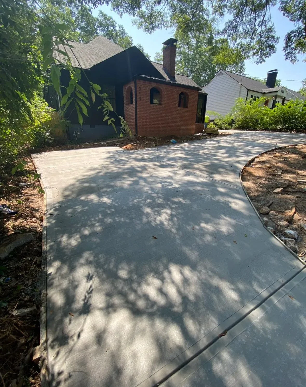 Newly poured concrete driveway leading to a brick house surrounded by trees and neighboring houses.